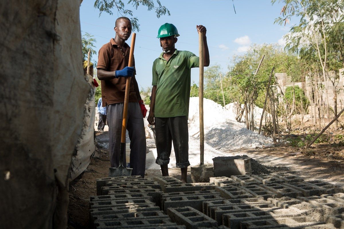 Elias Jean Oriel (left) and Regala Laisse Moi turn sand and cement into cinderblocks in the Canaan 2 section of Canaan, Haiti. "There are four types of block for different building needs," says Oriel, who is making wall block, known as "type 15," which sells for 25 gourds each (about 50 cents). This particular batch will go to expand Oriel's own house nearby, which he's been building for the past four years. Image by Allison Shelley. Haiti, 2018.