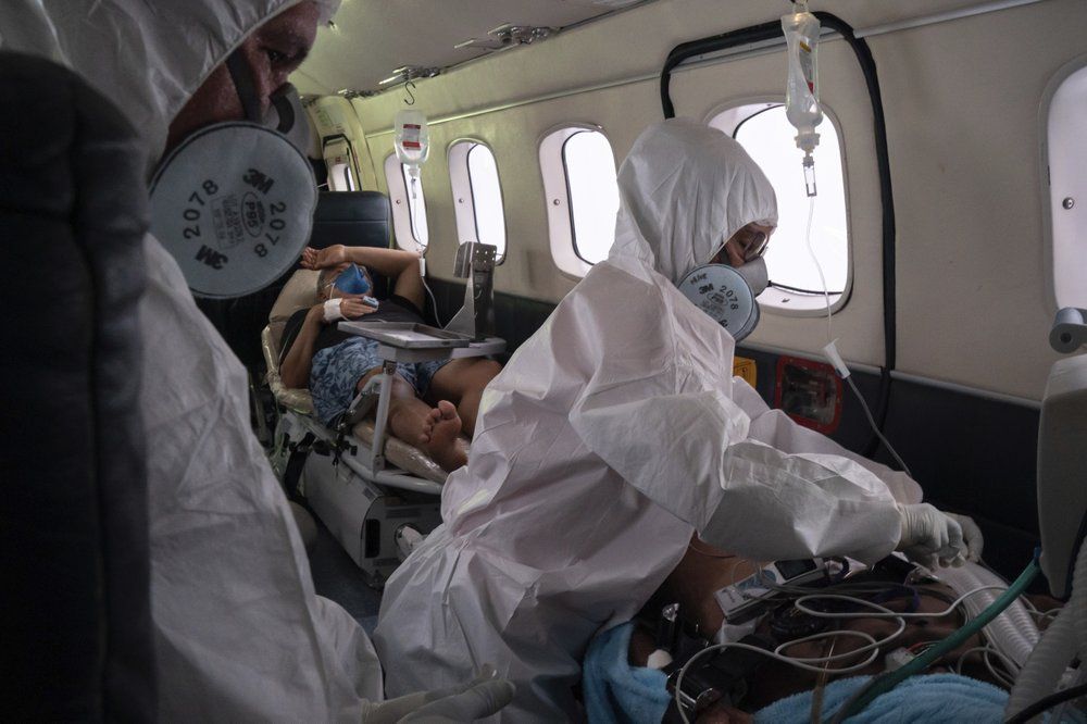 Doctor Daniel Siqueira, left, and nurse Janete Vieira monitor COVID-19 patients Abraão Lasmar, left, and Sildomar Castelo Branco onboard an aircraft as they are transferred from Santo Antônio do Içá to a hospital in Manaus, in Brazil's Amazon state, Tuesday, May 19, 2020. Image by AP Photo/Felipe Dana. Brazil, 2020.