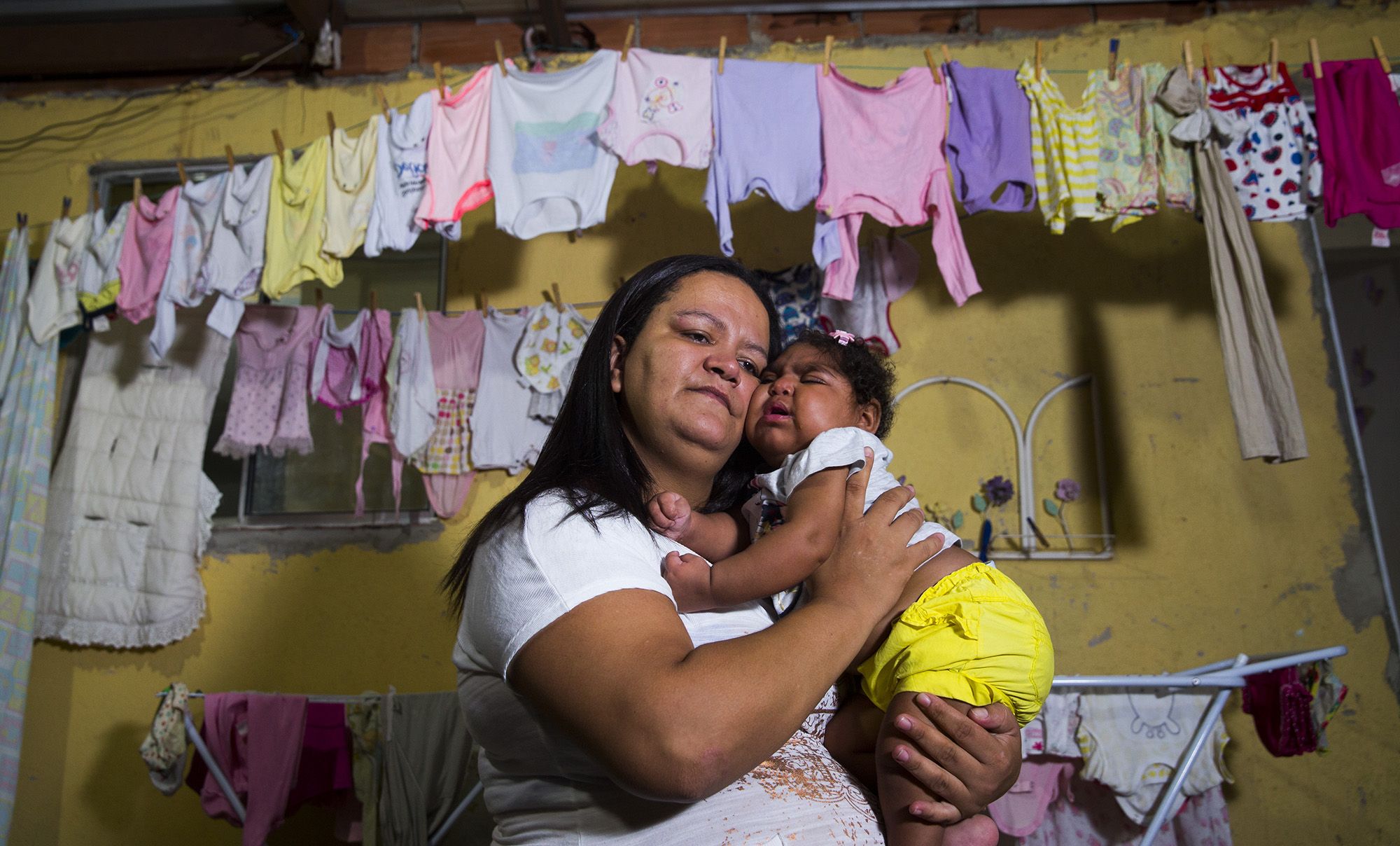 Fabiane Lopes holds her daughter, Valentina at their home in Duque de Caxias, a suburb of Rio de Janeiro in southeastern Brazil. Valentina's mother was pregnant when she became infected with the Zika virus and her daughter was born with microcephaly—a congenital malformation with smaller than normal head size for age and sex as well as other profound birth defects. Brazil has confirmed far more malformations of the brain in babies born to mothers who were infected with Zika than any other country. After she gave birth to Valentina, she elected to have a tubal ligation so she could not become pregnant again. Image by Mark Hoffman. Brazil, 2017.