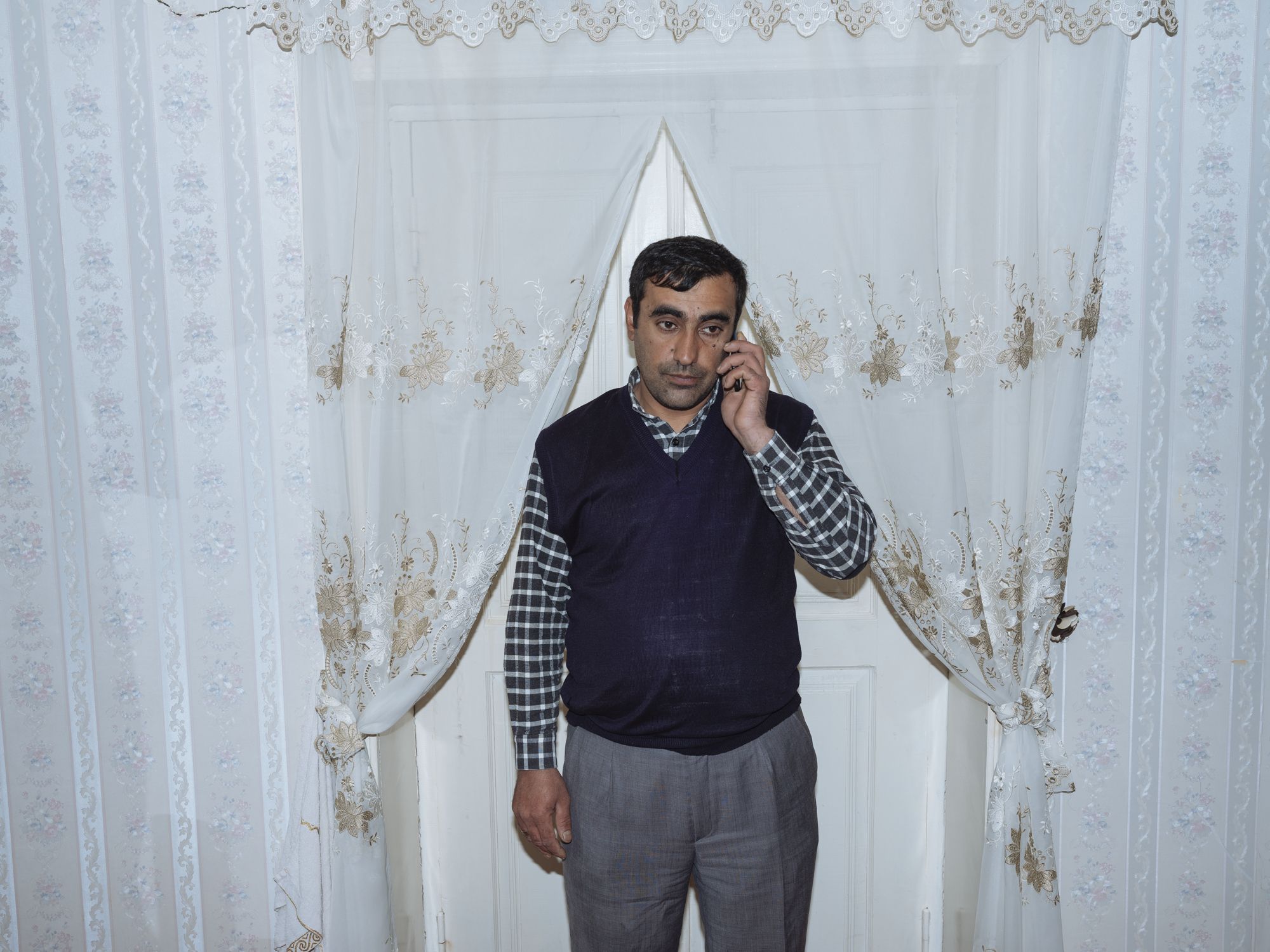 Behruz, 36, a telephone line repairer, speaks on the phone at his home in Sivu village.

Like lots of men in rural areas, Behruz's father works in Russia for significantly higher wages. The wives of such migrant workers must then not only work in farm production but also maintain their homes and raise their children. Image by Emin Ozmen / Magnum Photos. Azerbaijan, 2018.