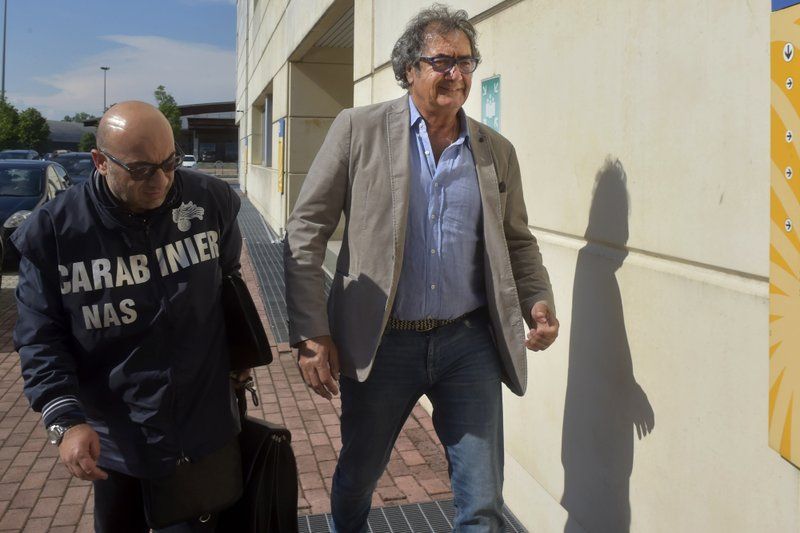 Dr. Guido Fanelli, right, is taken to the Carabinieri headquarters in Parma, Italy, for questioning in an alleged pharmaceutical kickback scheme on Monday, May 8, 2017. That morning, police jolted Fanelli out of bed. It was a spectacular fall from grace for a man who appeared days before on a popular television show to promote painkillers. Image by AP Photo/Marco Vasini. Italy, 2017. 