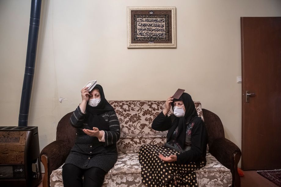 65-year-old Roghayeh prays at her sister's home. To keep the distancing rules, the two watch religious ceremonies on television and hold the Koran over their heads and ask for forgiveness. Roghayeh usually imports women's clothing from Turkey. But during their last trip there, the border was closed because of the pandemic, and their goods have remained in Turkey. Roghayeh had to pay the high cost of cancer treatment and burial for her late husband on her own. Inevitably, she continues to run her small shop in Tabriz to service loans. Image by Jalal Shamsazaran / NVP Images. Iran, 2020.