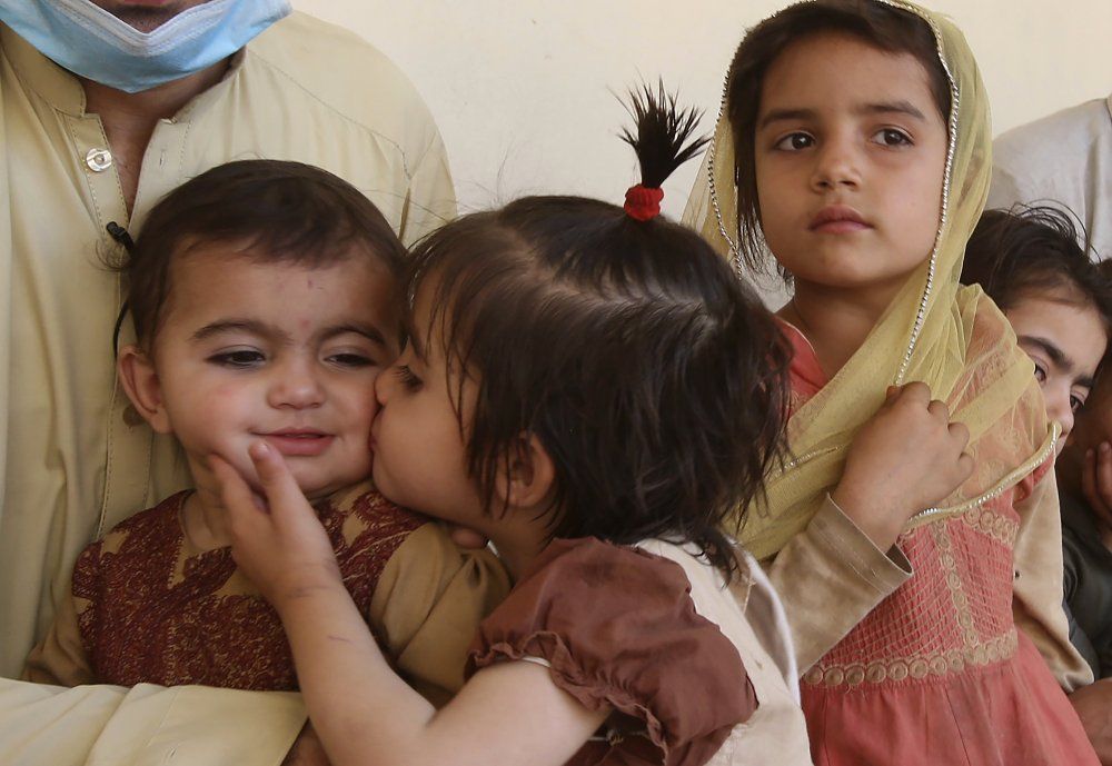 In this May 6, 2020 photo, Tariq Nawaz holds his 10-month-old baby daughter Tuba who suffers from polio, as a sister kisses her, in Suleiman Khel, Pakistan. For millions of people like Nawaz who live in poor and troubled regions of the world, the novel coronavirus is only the latest epidemic. They already face a plethora of fatal and crippling infectious diseases: polio, Ebola, cholera, dengue, tuberculosis and malaria, to name a few. The diseases are made worse by chronic poverty that leads to malnutrition and violence that disrupts vaccination campaigns. Image by AP Photo/Muhammad Sajjad. Pakistan, 2020.