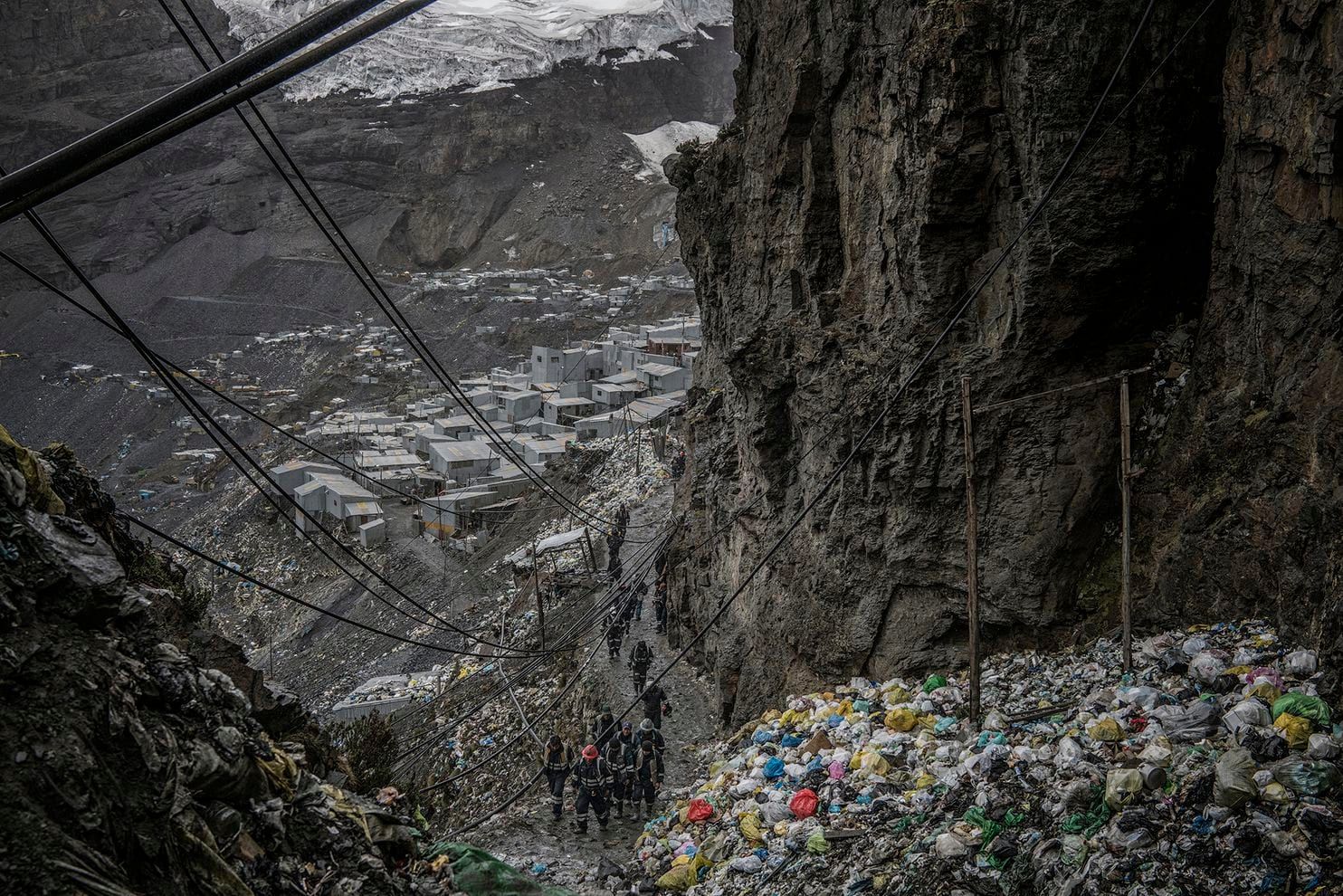 Workers return from the mines for lunch along a pathway etched into a cliff, past a mountain of garbage, at the La Rinconada gold mine complex in Peru. Peru,2019. Image by James Whitlow Delano.