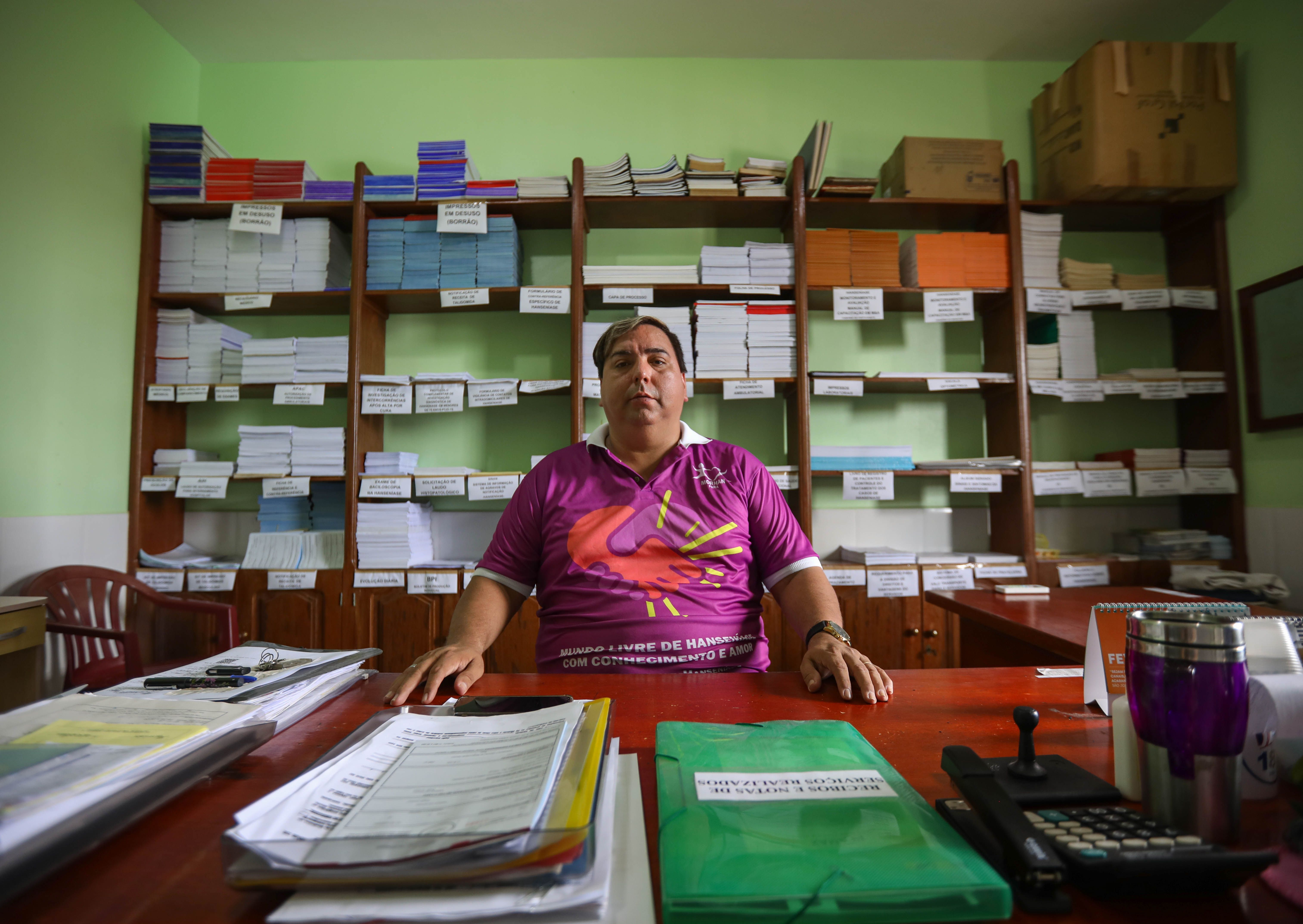 Edmilison Picanco, president of MOHAN in Pará, sits at his desk at the Center of Dermatology in Marituba. As the son of two leprosy patients, Picanco is leading the campaign demanding federal reparations for the children of these patients. Image by Anton L. Delgado. Brazil, 2020.