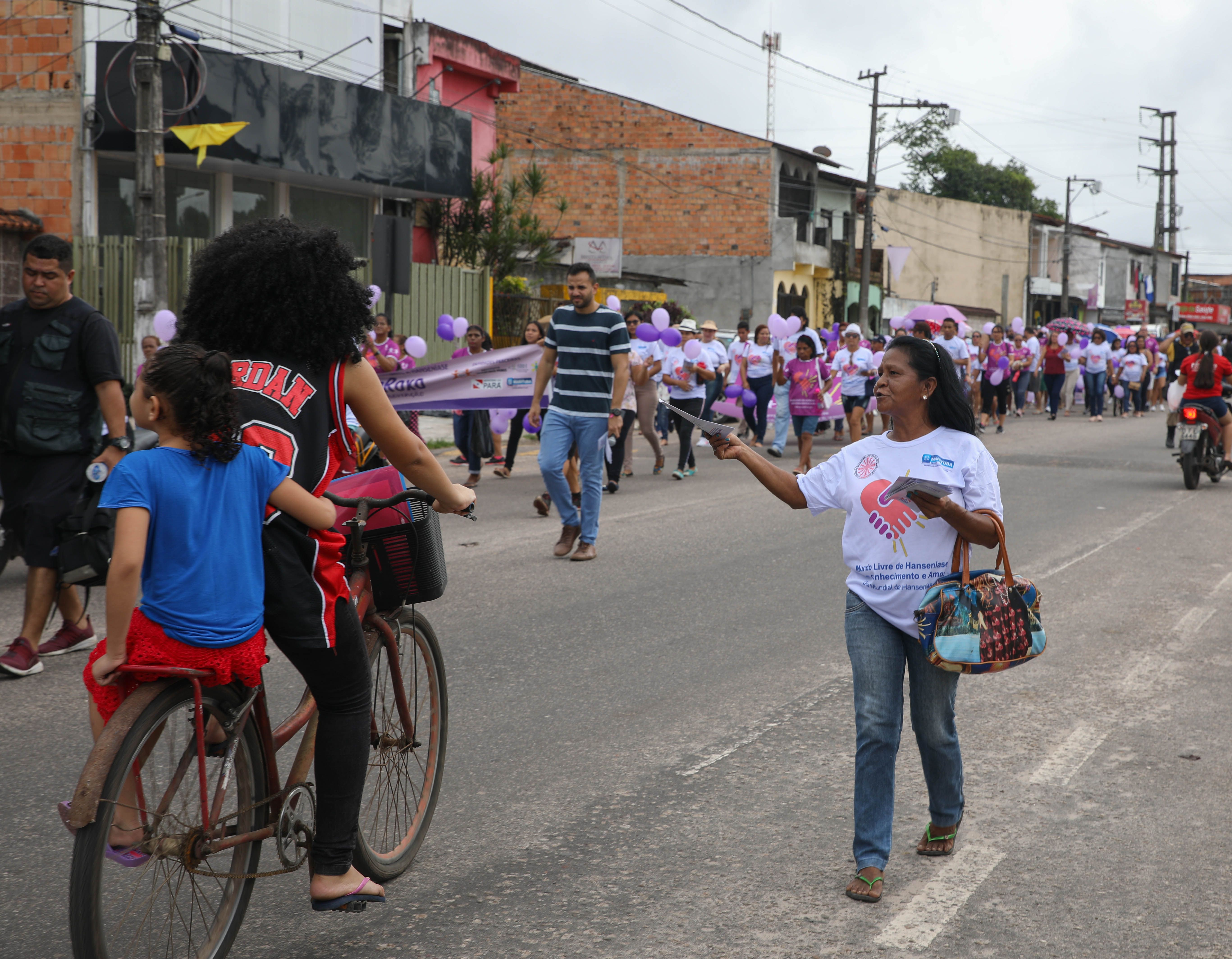A MOHAN volunteer holds out an informational brochure to a passing bicyclist during a leprosy awareness march in Marituba. Image by Anton L. Delgado. Brazil, 2020.