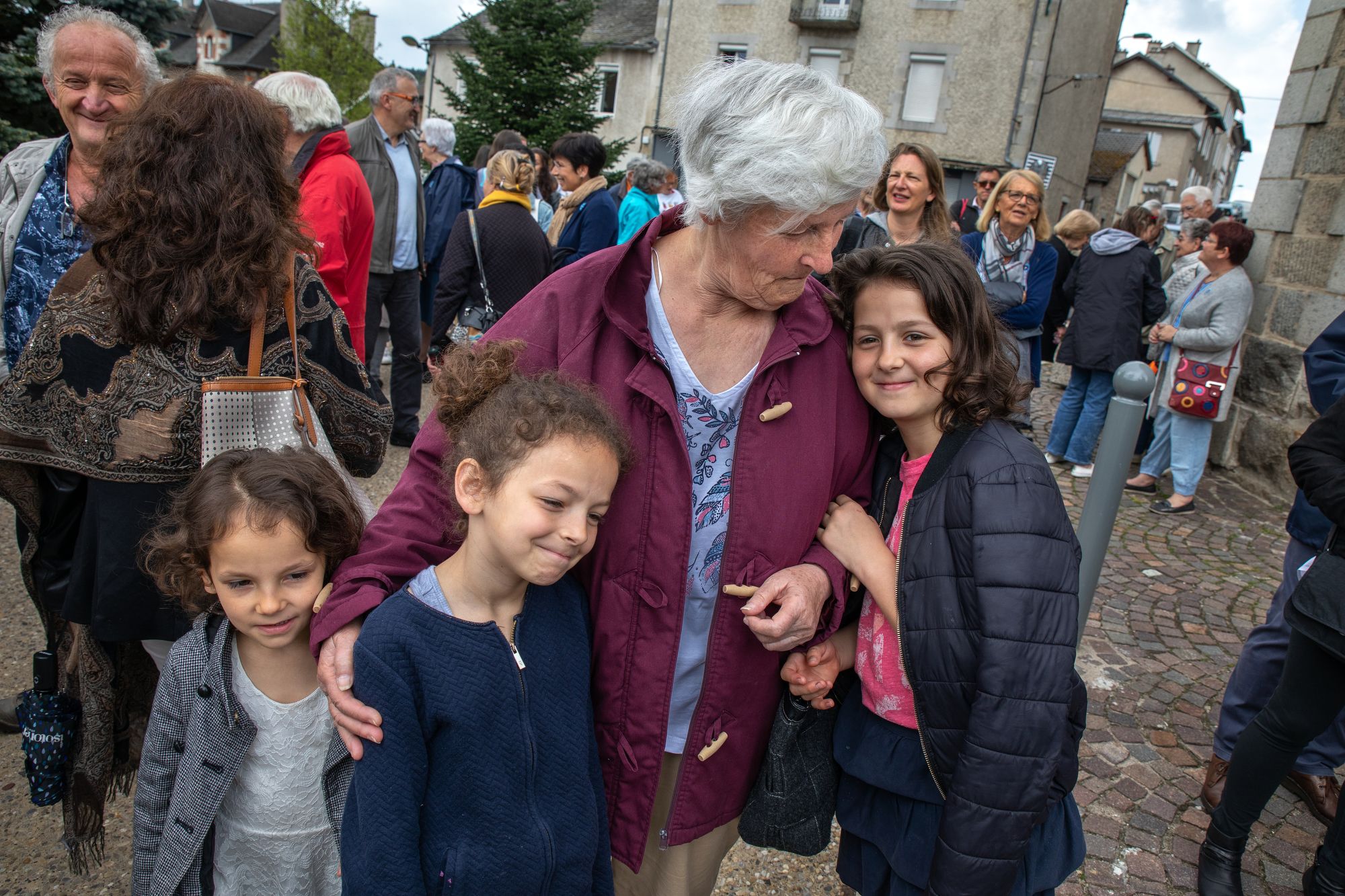 Michelle Baillot brings Touana (5), Schkourtessa (7) and Erlina Sélimi (10) to France’s World War II Victory Day at Le Chambon-sur-Lignon’s town’s square.  The girls are from a Kosovar refugee family that Baillot has been close to now for ten years. “I tell them that you are not from here, so you are going to have to be better than everyone else.” Image by Lucian Perkins. France, 2018.