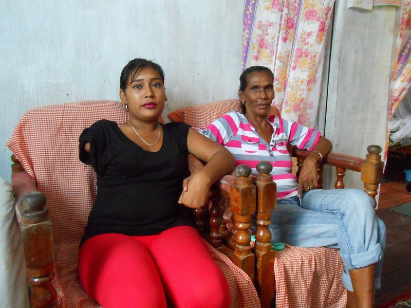 Natasha Houston and her mother at home in Zeelgult. In 2013, Houston's husband killed their two children, slashed her arm and hand, then died, apparently by suicide. Image by William Rawlins. Guyana, 2018.
