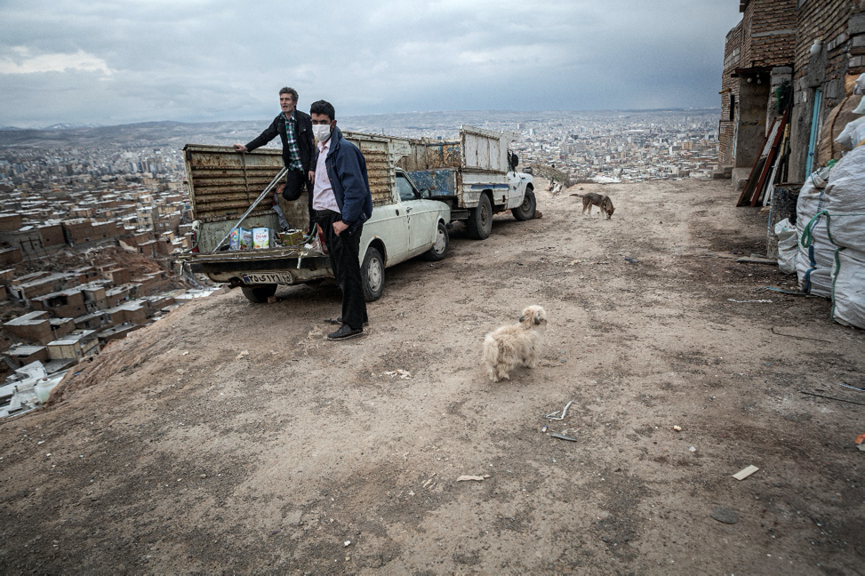 Tabriz, Iran, April 26, 2020. They are disembarking the waste from the car. The main job of many suburb dwellers of Tabriz is the waste trade and they are living in this way. For the large number of Iranians who live on a day-by-day income, staying home means having no money to pay for essential things such as food. Therefore, they must take their life in their own hands and work in order to survive even at the risk of getting infected, spreading the virus in society at large, and even getting fined for breaking the quarantine. For them, choosing either path has extreme consequences.  Image by Jalal Shamsazaran / NVP Images. Iran, 2020.