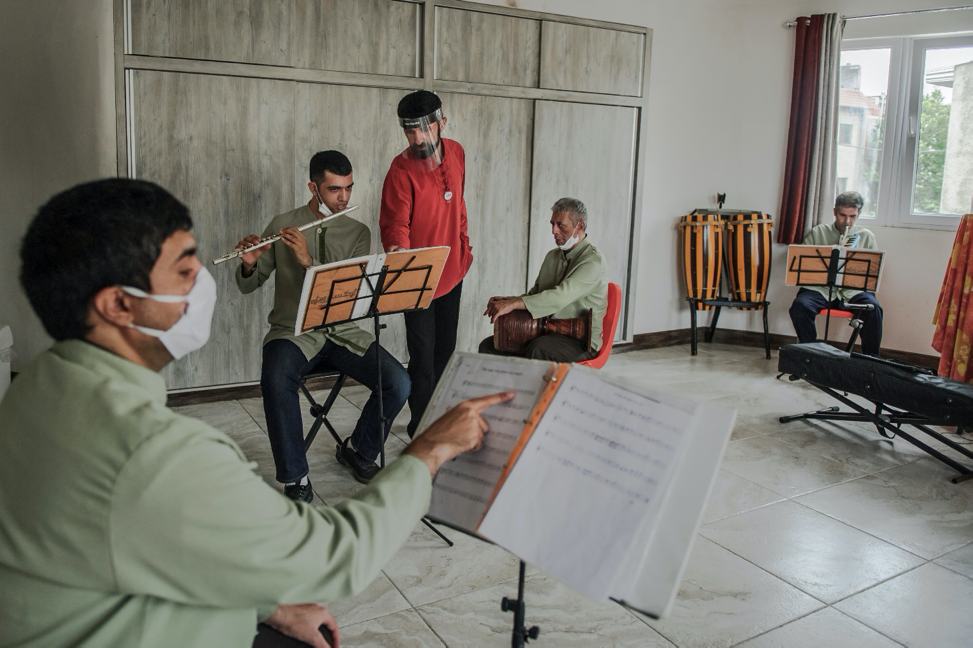 Gorgan, Iran - June 6, 2020 : Mehdi Alaie, 39, while instructing music to his trainees, is using a protection shield since three children in the Behkoush center have been died so far because of the coronavirus infection. Although he does not have any permanent job and working as a music instructor for children provides him with only an approximate hourly wage of four dollars, he has been working with the Behkoush center as a permanent instructor for almost five years. The Behkoush center is one of the most celebrated educational centers for mentally ill people in Iran which instructs these people in varied areas and improves their abilities for the better life. Boys aged 10 years and older diagnosed with any types of mental and physical disabilities are accepted here and would be instructed in a variety of fields from basic learnings such as shapes and currencies recognition to professional learnings as mathematics, carpet weaving, woodworking, playing musical instruments, and theatre acting. Then they would be introduced to the job market in order to find a convenient carrier. Although three trainees passed away due to the coronavirus infection, the Behkoush center has resumed opening with almost less than ten percent of its capacity to provide services to the ones who are in immediate need. Image by Mahdi Barchian / NVP Images. Iran, 2020.