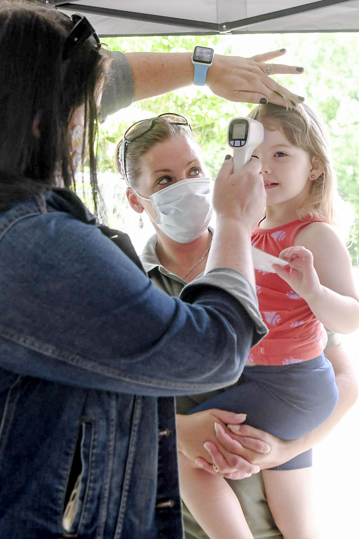 CANDLER, NORTH CAROLINA - Amy Waddell holds her daughter, Aliza, 3, as her temperature is checked before spending the day at Montmorenci United Methodist Church's daycare June 23, 2020. Image by Angela Wilhelm/Asheville Citizen Times/ North Carolina News Collaborative. United States, 2020.