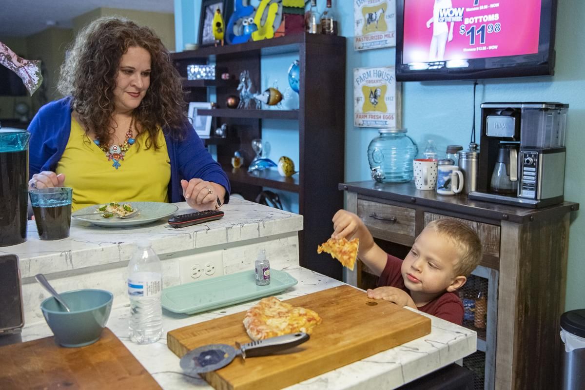 Crystal Camacho finishes her dinner at the kitchen counter as her son, Elias, 4, grabs a second helping of pizza on June 30, 2020 at their home in Swannanoa. Before finding a new day care for Elias after the one he was attending closed, Camacho and her husband had to take turns staying home half days or take the kids to work with them. Image by Angeli Wright/Asheville Citizen Times/North Carolina News Collaborative. United States, 2020.