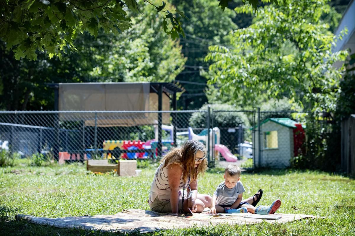 Bell's School teacher Angela Mehaffey reads a book with Elliot Fink, 2, on a blanket outside the Fletcher preschool June 22, 2020. Image by Angeli Wright/Asheville Citizen Times/North Carolina News Collaborative. United States, 2020.