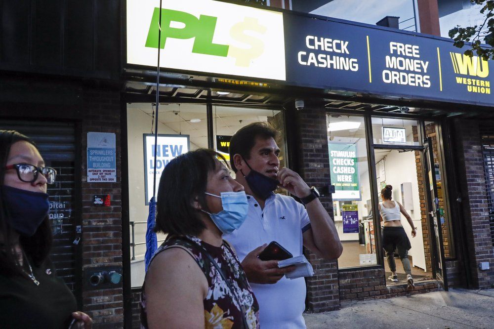 Magnolia Ortega, center, stands outside a Western Union with her husband Arturo Morales and their daughter Marlene after wiring money to her family in Mexico, Wednesday, June 24, 2020, in Staten Island, New York. Ortega lost her job cleaning houses amid the COVID-19 pandemic, reducing the monthly amount she sends home. She's considering returning to her hometown of San Jeronimo Xayacatlan but says there's no work there either and that would mean one less family member sending back one less monthly check. Image by John Minchillo/AP Photo. United States, 2020.