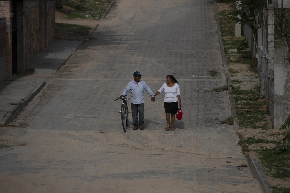 A couple walks hand in hand through San Jeronimo Xayacatlan, a town in Mexico from where nearly a third have emigrated to New York, Friday, June 26, 2020. After a generation of emigration, the quality of life has improved here and there's less urgency for a decision "that means going far from everything, starting a new life, watching your children grow from far away," said town historian Tamara Cardoso. Image by Fernando Llano/AP Photo. Mexico, 2020.