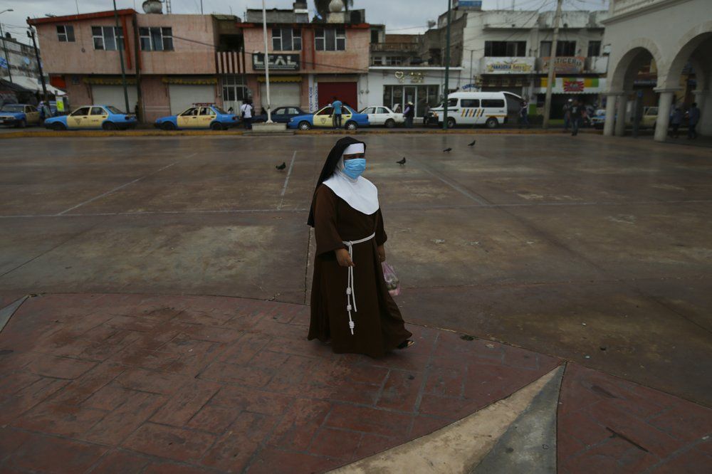 A nun wearing a mask amid the COVID-19 pandemic walks at the main square in Acatlán de Osorio, a town in Mexico where the life blood is remittances from locals who have emigrated, Thursday, June 25, 2020. Mexican migrants sent home a record $4 billion in March. After a dip in April, numbers were strong again in May. Image by Fernando Llano/AP Photo. Mexico, 2020.