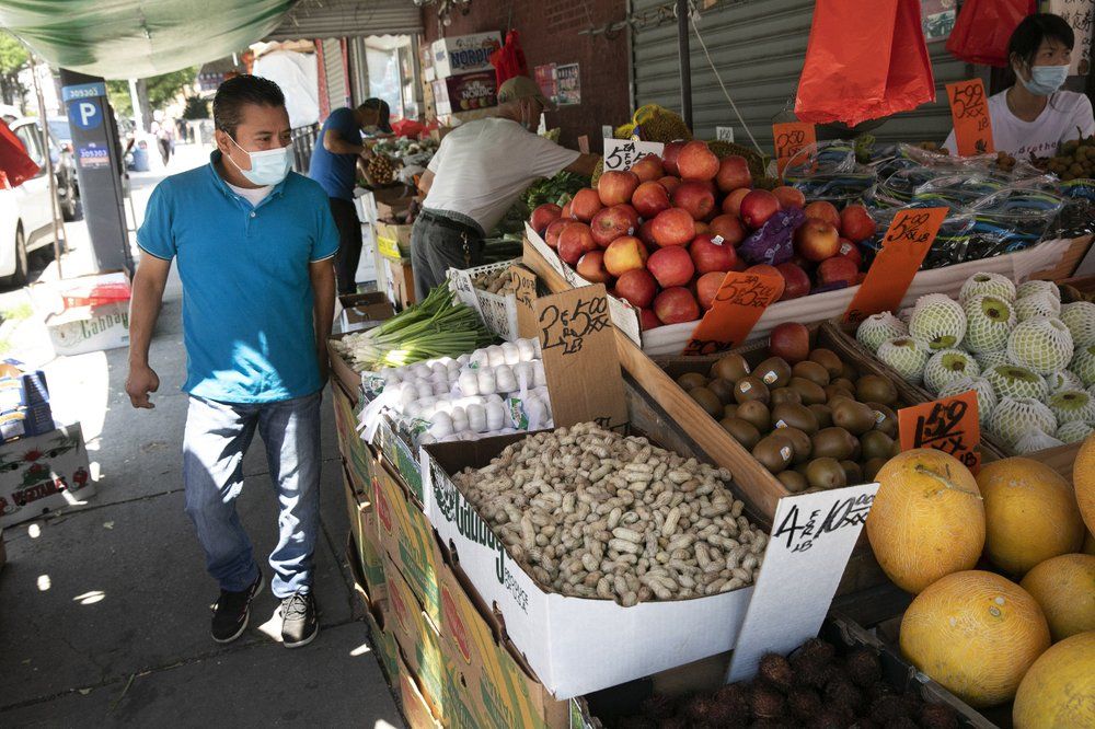 Axayacatl Figueroa, who recovered after suffering from COVID-19, walks by a neighborhood food stand in Brooklyn, New York, Monday, July 6, 2020. Figueroa, who emigrated to New York in 2005 from Mexico's San Jerónimo Xayacatlán, leaving behind his wife and son, recovered after three weeks, but lost his full-time job in the kitchen of a Vietnamese restaurant and returned part-time. Before coronavirus, he sent up to $400 home every month. Image by Mark Lennihan/AP Photo. United States, 2020.