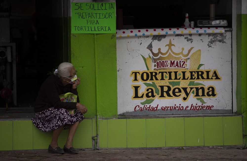 A woman sits next to a tortilla shop in Acatlán de Osorio, a town in Mexico where the life blood is remittances from locals who have emigrated, Thursday, June 25, 2020. Those who went from Mexico to live in the U.S. are worried about how to keep supporting their families amid lay-offs due to lockdowns to contain the COVID-19 pandemic. Image by Fernando Llano/AP Photo. Mexico, 2020.