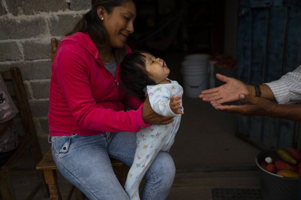 Nataly Ortega, whose mother Magnolia Ortega works cleaning homes in Staten Island, New York, holds her niece Azul in San Jeronimo Xayacatlan, Mexico, Wednesday, June 24, 2020. Nataly's uncle recently had a telephone installed so they can stay in touch with Nataly's mother, whose cancer is in remission, but remains vulnerable to COVID-19. Image by Fernando Llano/AP Photo. Mexico, 2020.