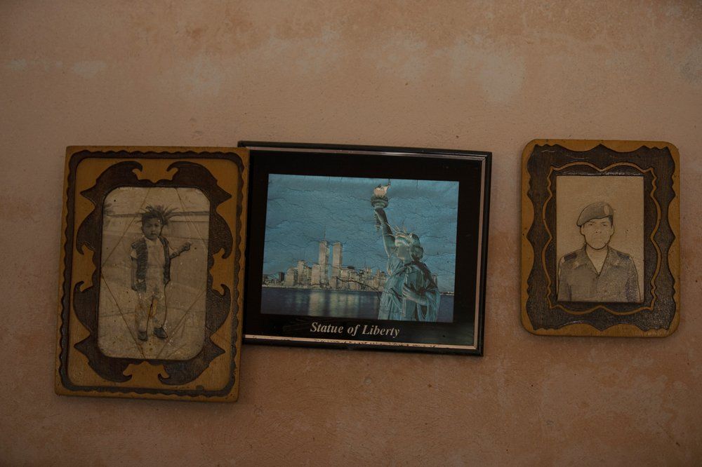 Photographs of Jorge Vazquez, left, and his brother Orlando Vazquez flank an image of the Statue of Liberty in New York, inside the home of their mother Catalina Vazquez in San Jeronimo Xayacatlan, Mexico, Thursday, June 25, 2020. Catalina's family has used the money sent back from her adult children, who have all worked on and off in New York and California, to add rooms to the house, build a kitchen where modern appliances coexist with a cooking fire and corn-grinding stone, buy her medicine and pay for one of her granddaughter's to study psychology. Jorge returned home from New York, while Orlando remains in California. Image by Fernando Llano/AP Photo. Mexico, 2020.