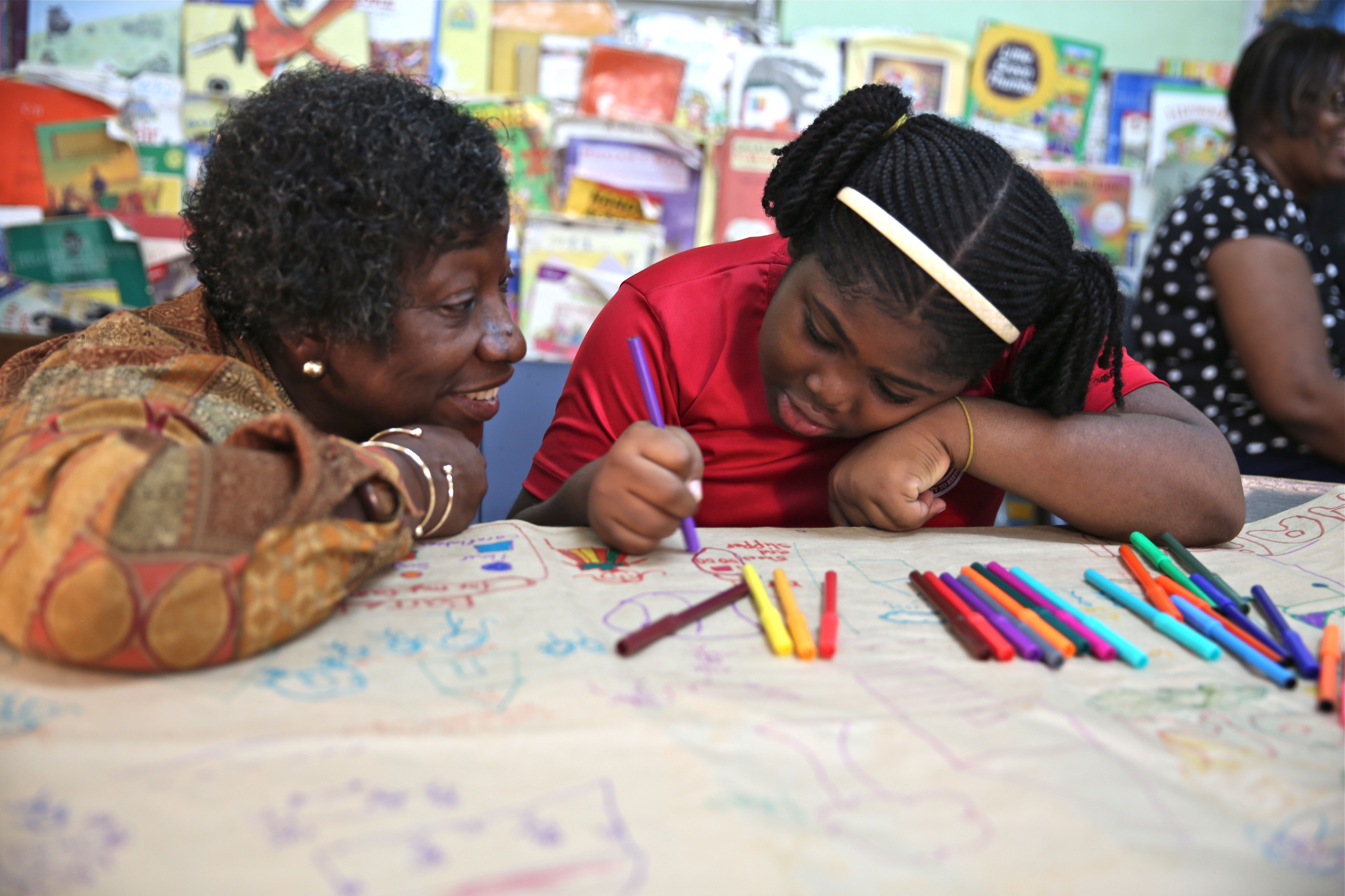 Dr. Claudette Crawford-Brown interacts with Shaniqua Long during an art therapy session at Shortwood Practising Infant, Primary and Junior High School in Kingston, Jamaica. Long's mother migrated to the United States. Image by Sabriya Simon. Jamaica. From Melissa Noel's Pulitzer Center-supported project, "Beyond The Barrels: How Migration Impacts Caribbean Children."