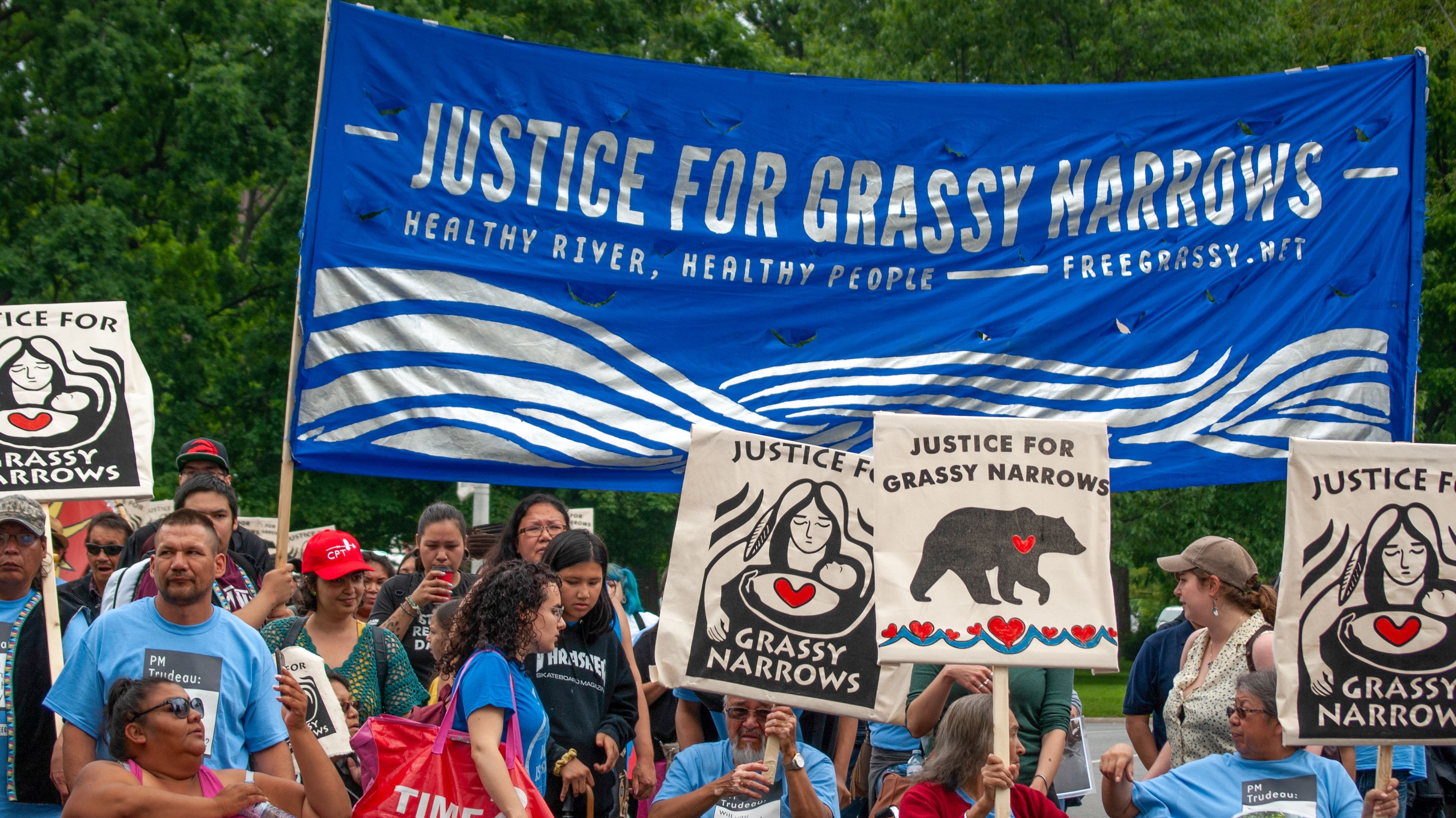 A group of Grassy Narrows First Nation residents and their supporters stand below a "Justice for Grassy Narrows" banner. Members of the Grassy Narrows First Nation traveled to Toronto to demand justice. Image by Shelby Gilson. Canada, 2019.