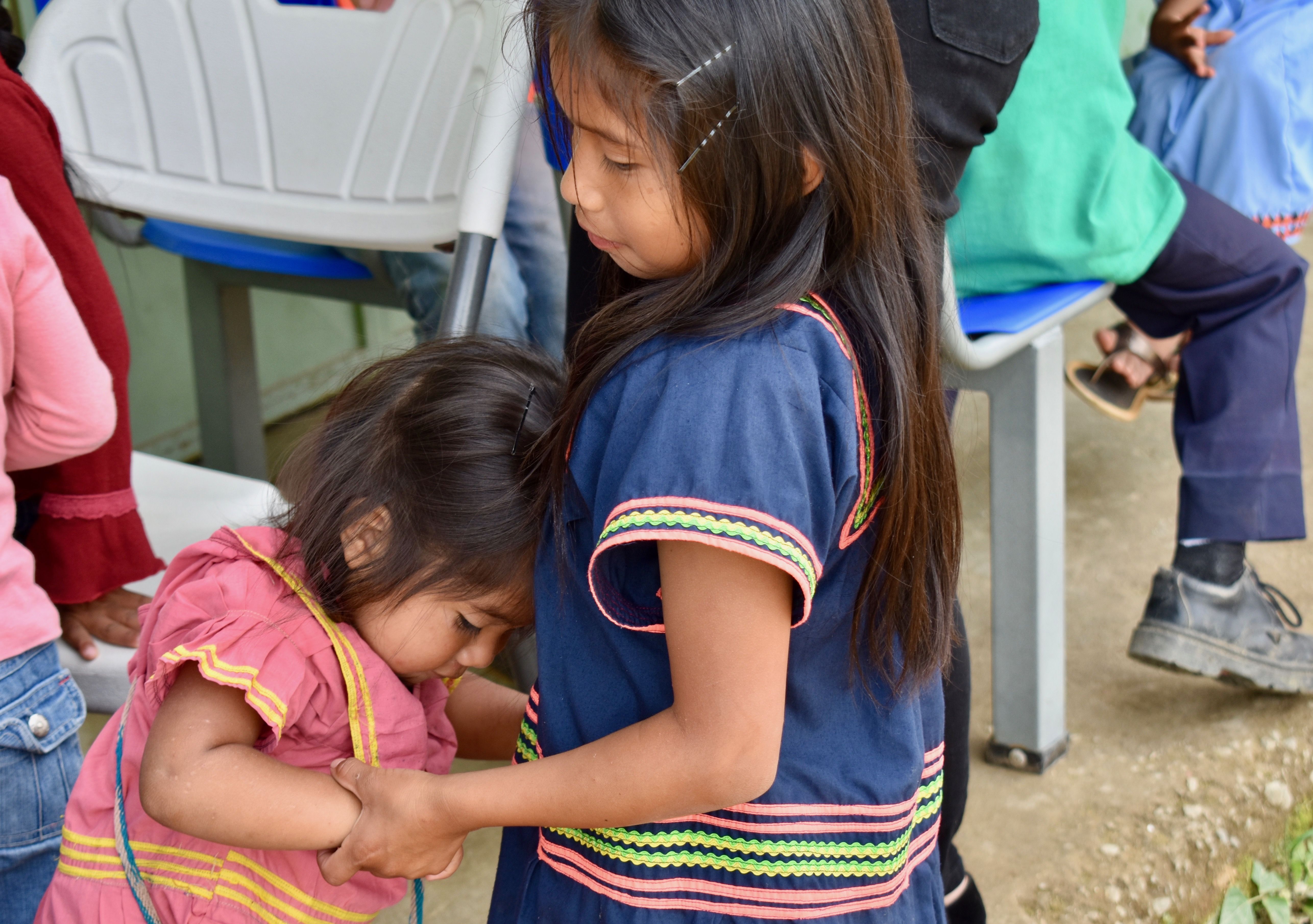 Distance and rural settings make access to larger cities difficult for some. A young girl leans on her sister after traveling several hours by foot to visit a health clinic in Las Mellizas, the largest town near their home. Image by Samira Tella. Costa Rica, 2018. 