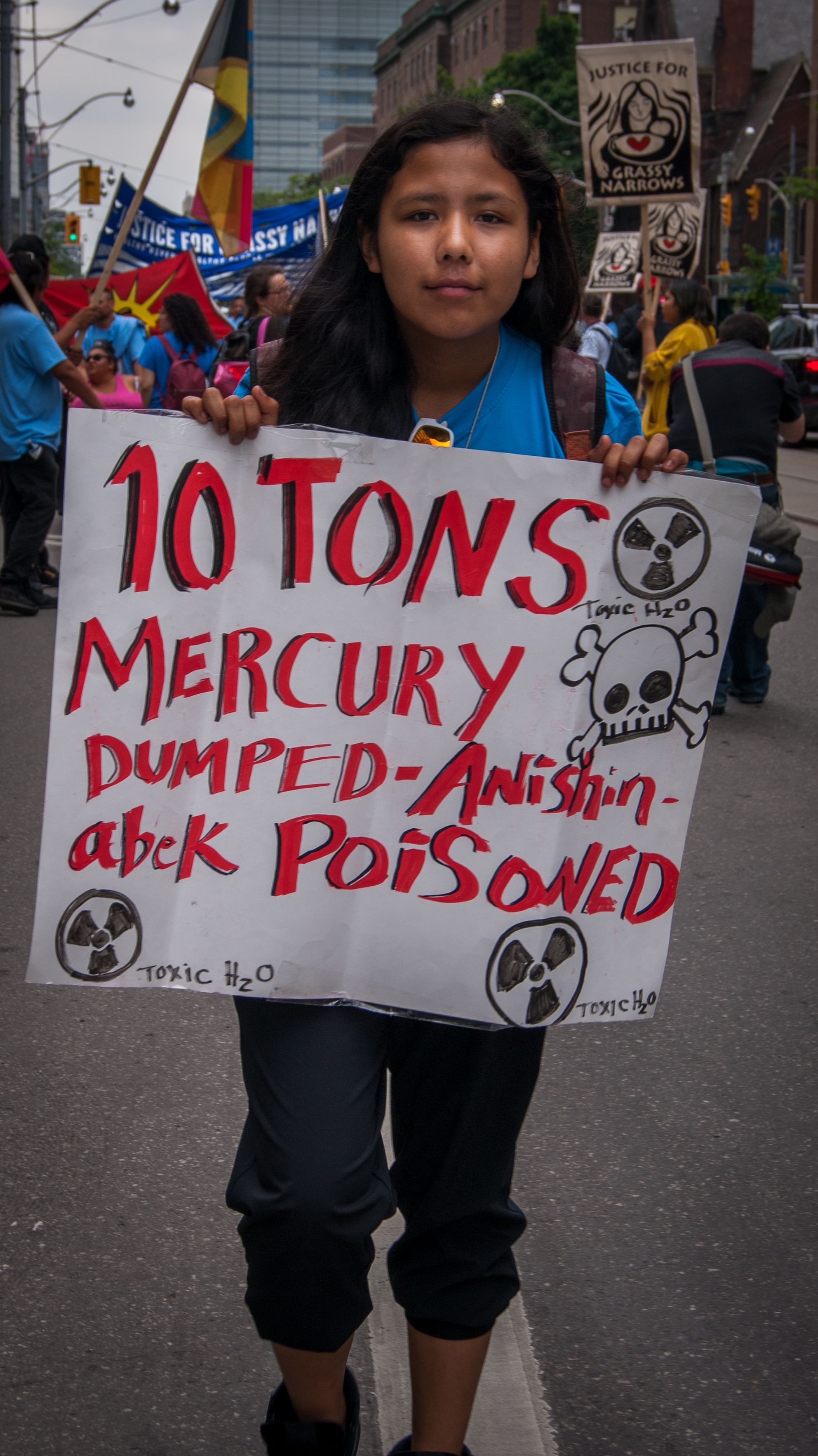 Paris Meekis poses with sign which reads, " 10 tons mercury dumped - Anishinabek poisoned." Image by Shelby Gilson. Canada, 2019.