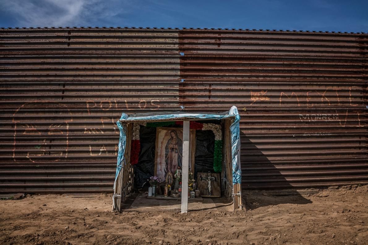 A Catholic shrine dedicated to the Virgin of Guadelupe is built right up against the U.S.-built border wall, by "Luis", a deportee from the U.S. who lives on his hilltop redoubt above Playas de Tijuana, Baja California, Mexico. What he and other deportees fear most are "coyote" traffickers or unknown migrants who prowl this hilltop either seeking to cross into the U.S. or who have more nefarious ambitions. Image by James Whitlow Delano. Mexico, 2017.
