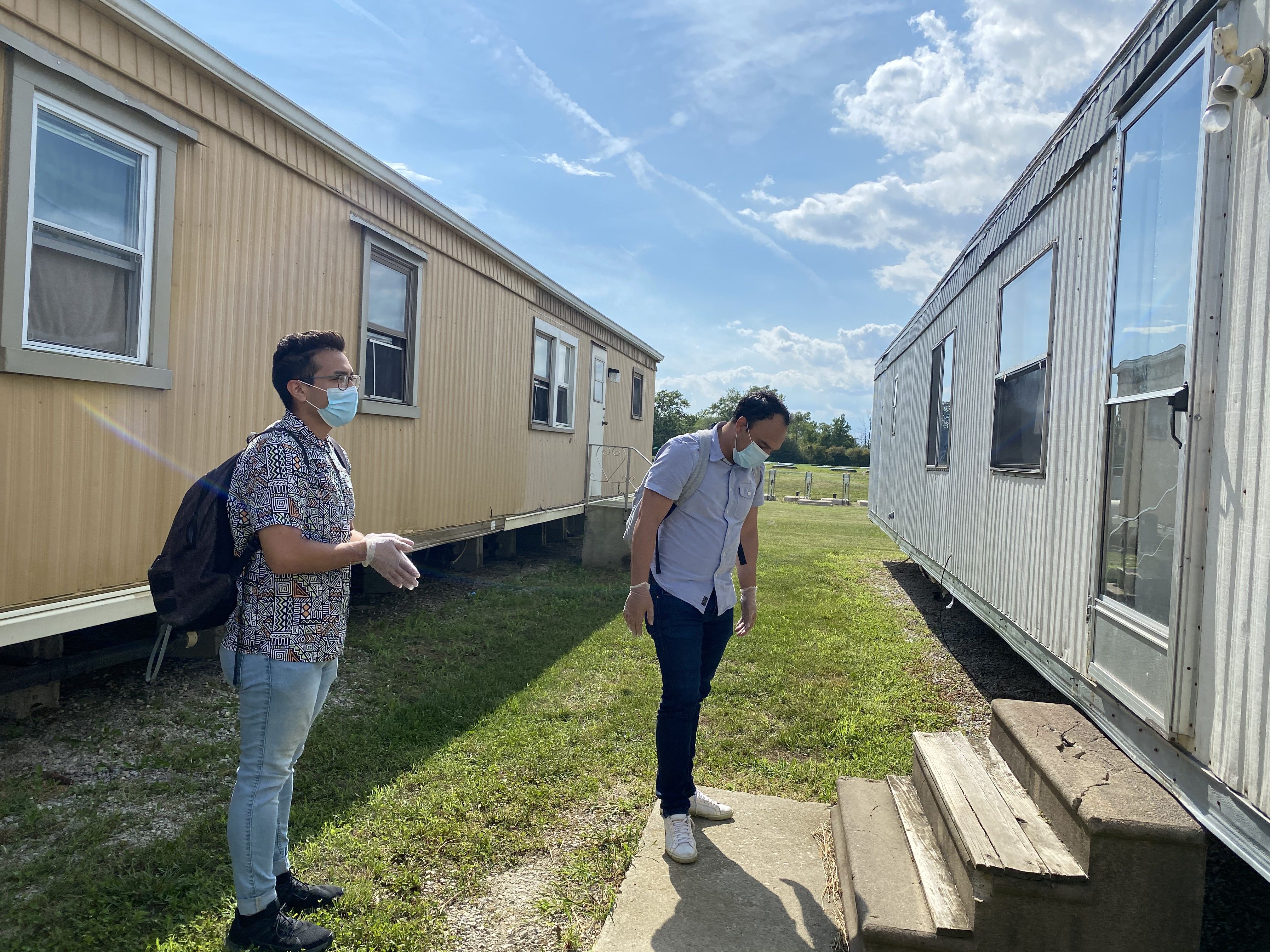 FLOC members Lorenzo Zamora (left) and Braulio Franco (right) wait outside for a farmworker to answer the door during their visit to Liskai Farms migrant camp. Image by Areeba Shah. United States, 2020.
