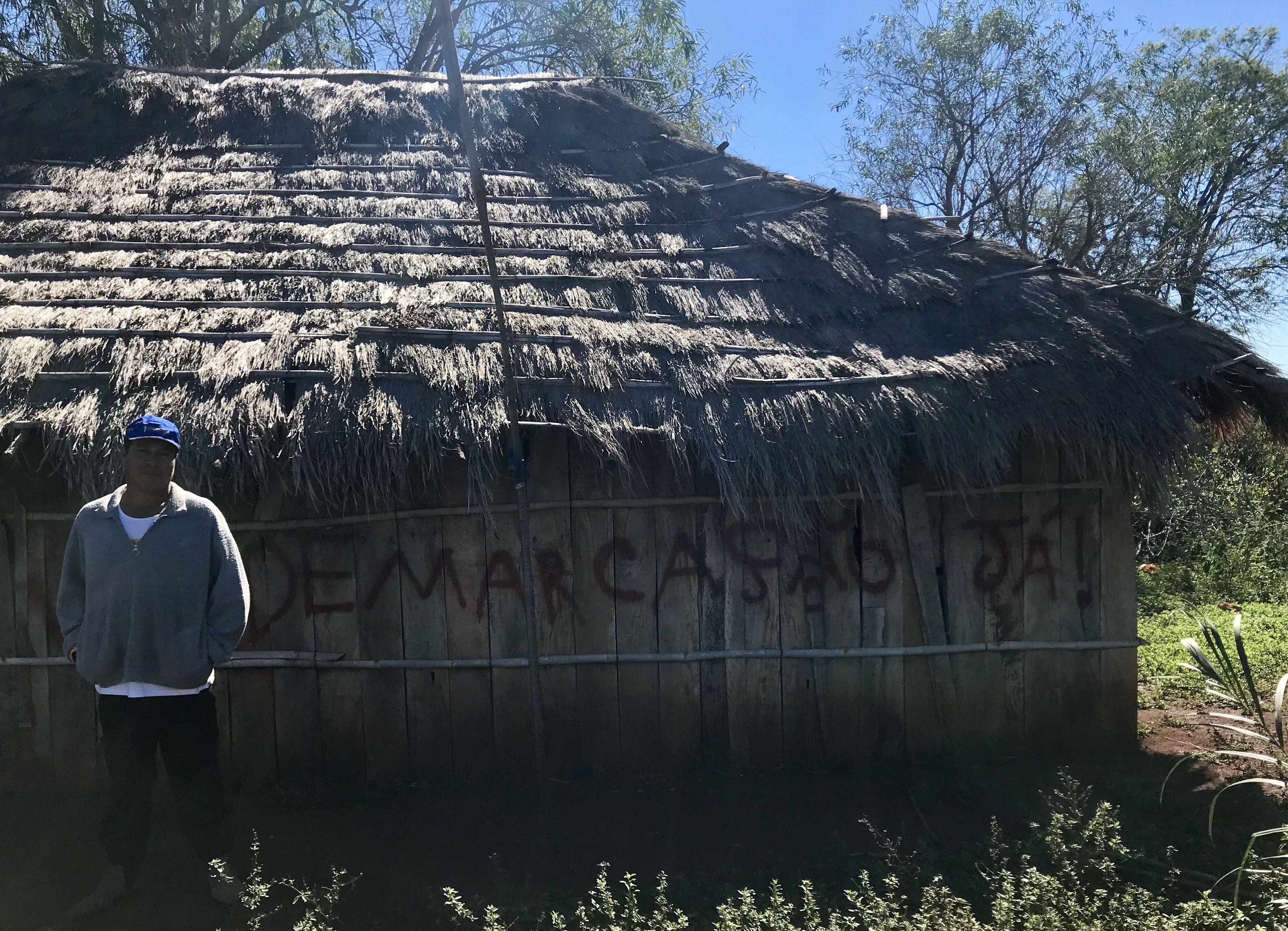 Cacique (or "Chief") Ezequiel João in front of the walls of his residence. "Demarcação Já!" (or "Demarcation Now!" is written as a form of protest to the government's long delay in demarcating and protecting the territories that were promised to his village. Image by Rafael Lima. Brazil, 2019.