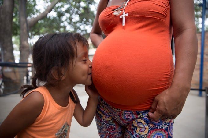 Venezuelan migrant Fabiana Correa Martinez, 4, kisses the belly of her pregnant mother Nairobi Correa Martinez in a migrant soup kitchen in Cucuta, Colombia on Feb. 9, 2019. Image by Megan Janetsky. Colombia, 2019.