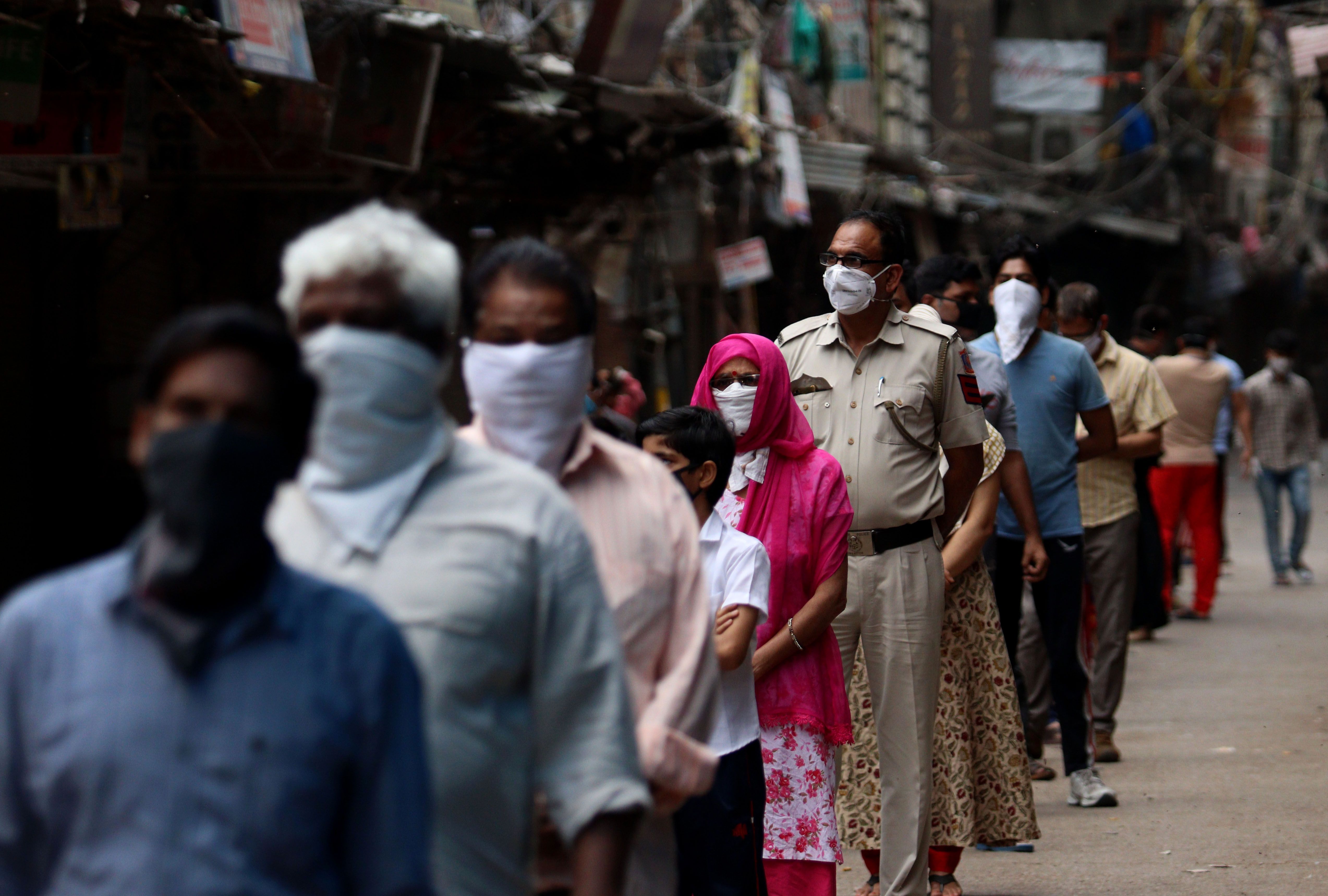 Mobile Covid-19 testing van in India. Delhi Police cop along with people stands in a queue for coronavirus test at Red Zone area, old Delhi. Image by Exposure Visuals / Shutterstock. India, 2020.