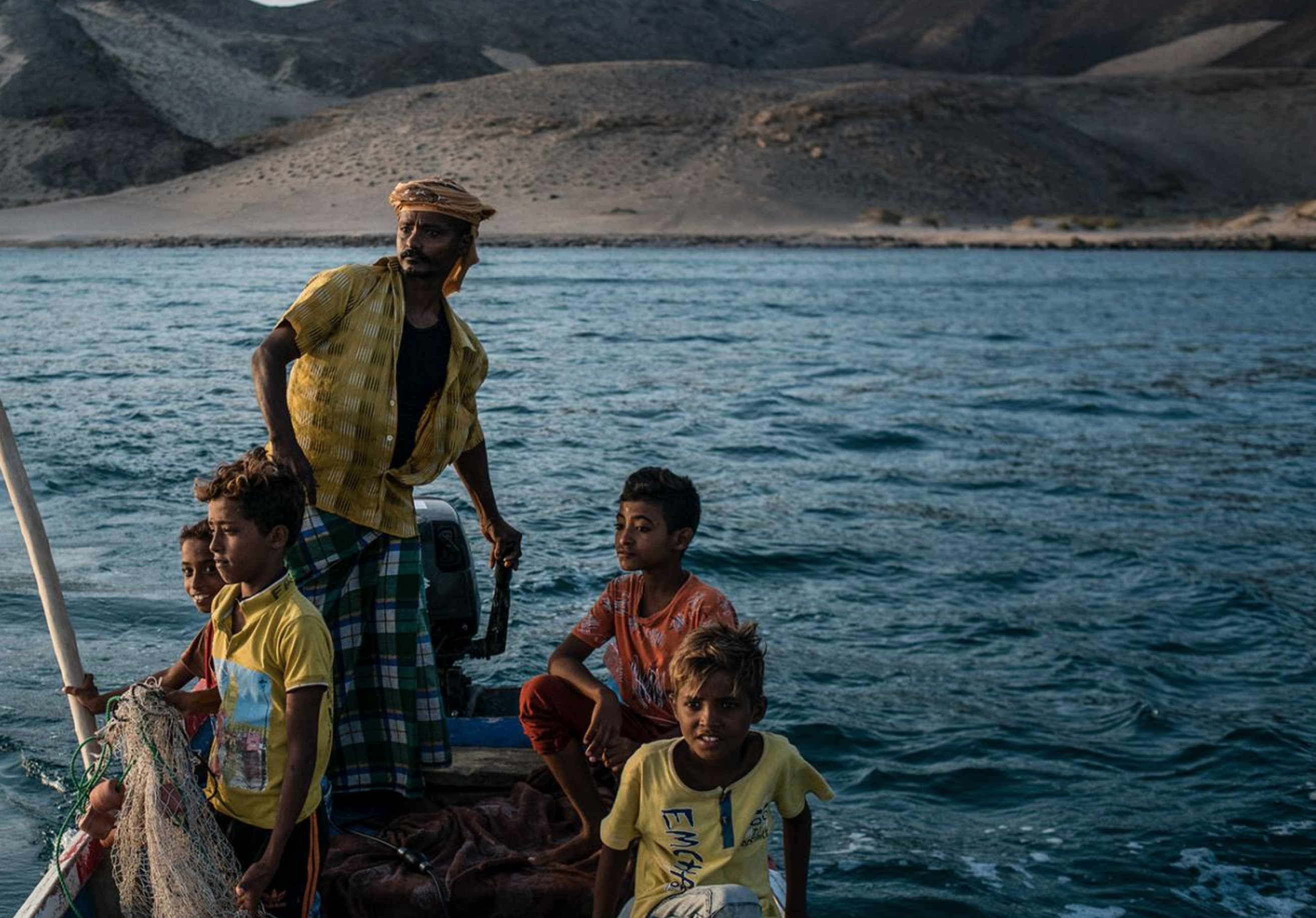 Shafai Saleh Hadi drives a friend's boat along the coast of Bir Fuqum, searching for fish with his sons. Image by Alex Potter. Yemen, 2018.