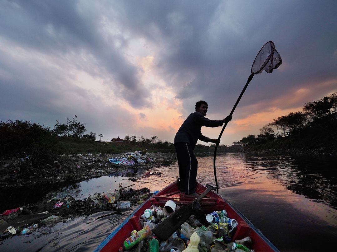 Deni Riswandani pushes his canoe filled with scavenged trash toward his village on the banks of the Citarum River. Demi travels up to eight miles a day on the polluted river to collect plastic and other recyclables. Image by Larry C. Price. Indonesia, 2016.