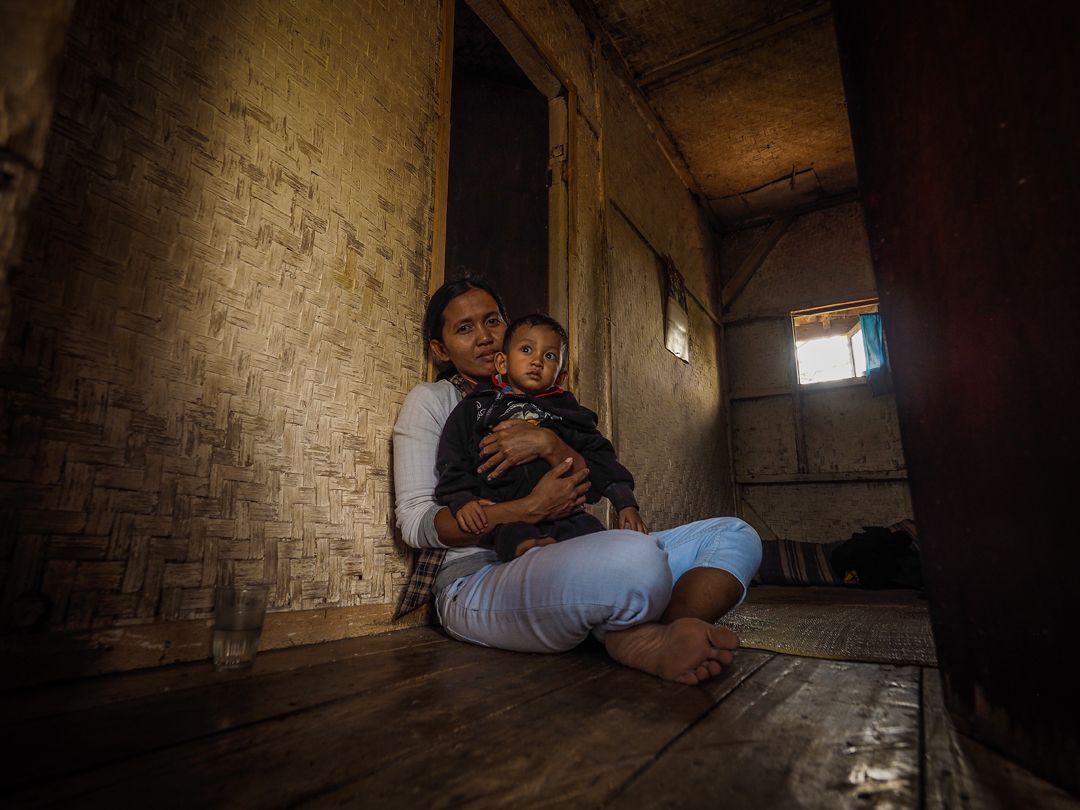 Risma, 36, holds her son Wati, 2, inside their bamboo home at Sukamaju, a tiny village surrounded by polluted rice fields irrigated with runoff from the textile factories at nearby Rancaekek. Image by Larry C. Price. Indonesia, 2016.