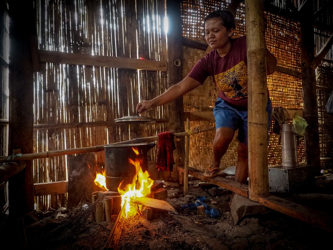 A woman tends a cooking fire inside her bamboo home at Sukamaju, a tiny village surrounded by polluted rice fields irrigated with runoff from the textile factories at nearby Rancaekek. Image by Larry C. Price. Indonesia, 2016.