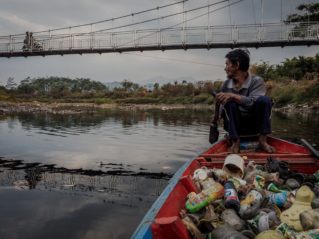 Deni Riswandani pushes his canoe filled with scavenged trash toward his village on the banks of the Citarum River. Demi travels up to eight miles a day on the polluted river to collect plastic and other recyclables. Image by Larry C. Price. Indonesia, 2016.