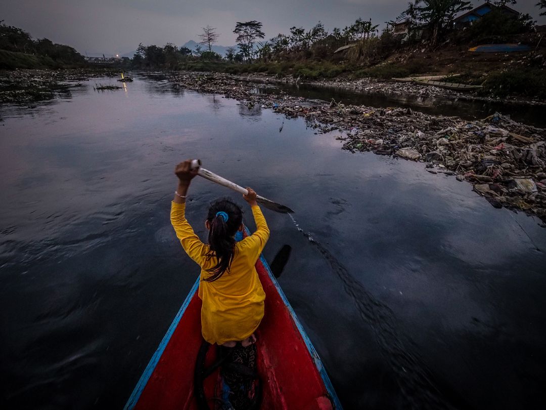 Rosi, 12, paddles her canoe at sunset past mounds of trash and garbage lodged against the banks of the Citarum River. Image by Larry C. Price. Indonesia, 2016.