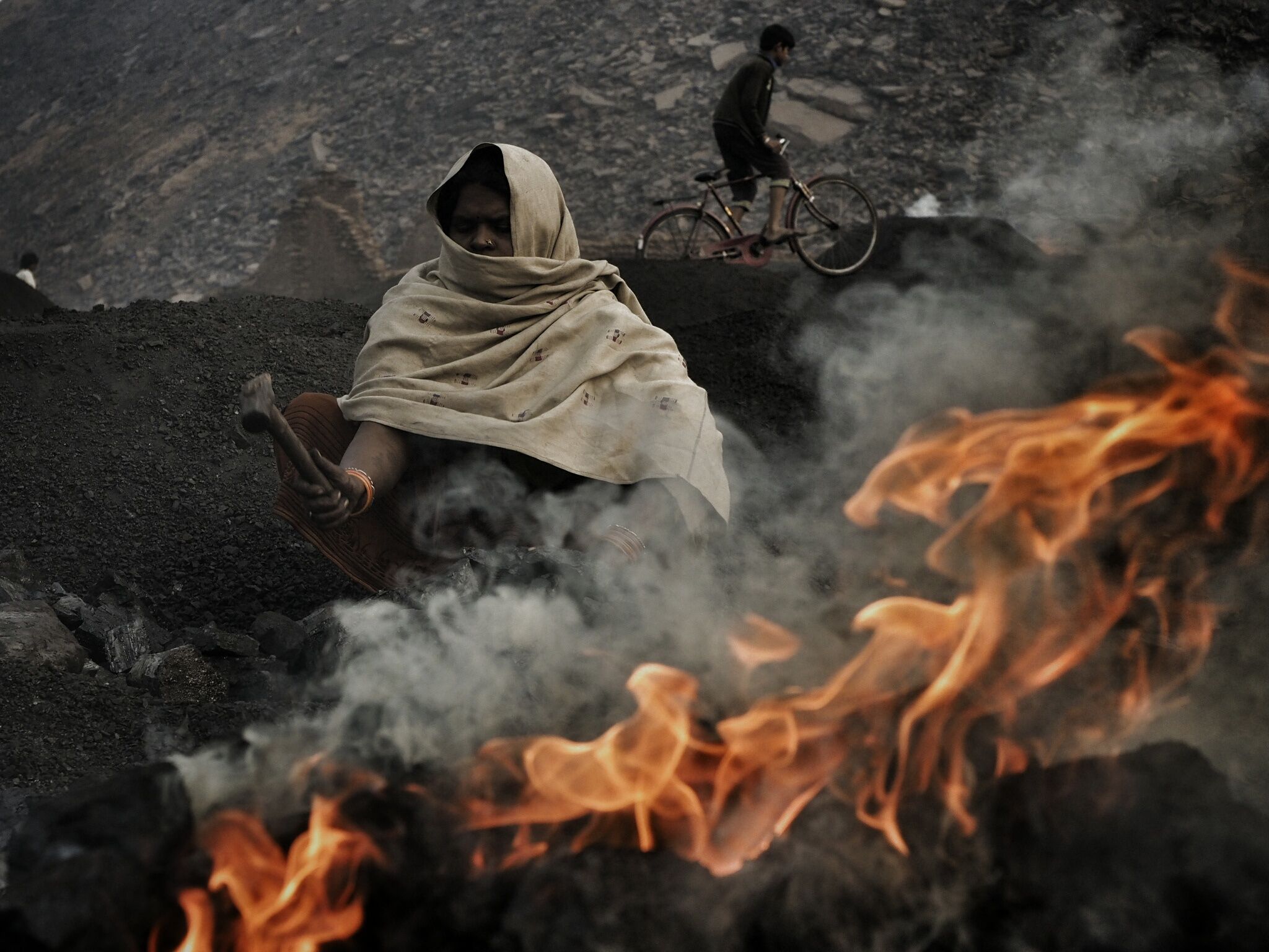 A woman tends a coal fire. 