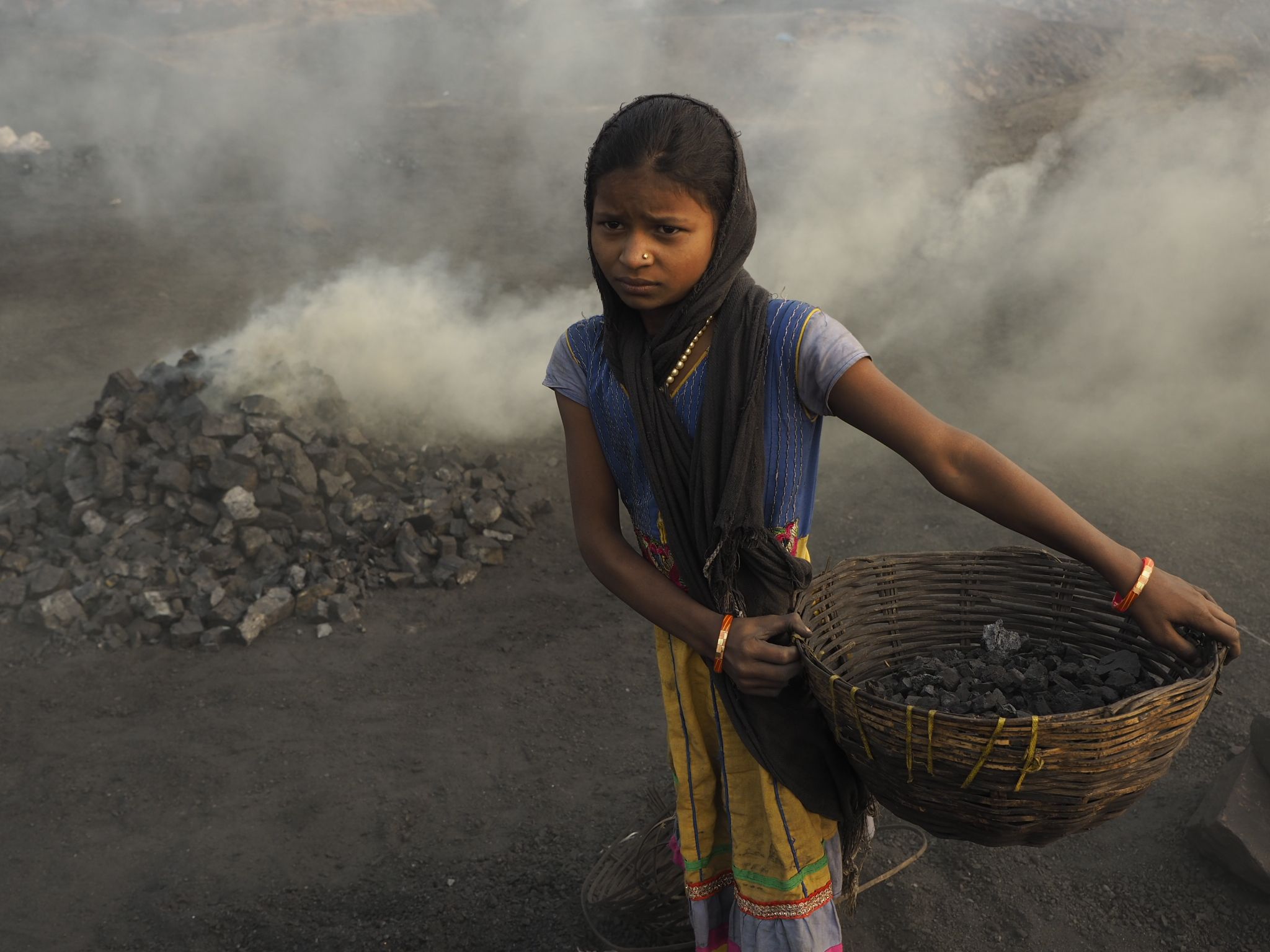 A young girls brings a basket of scavenged coal to a pile for burning into charcoal.