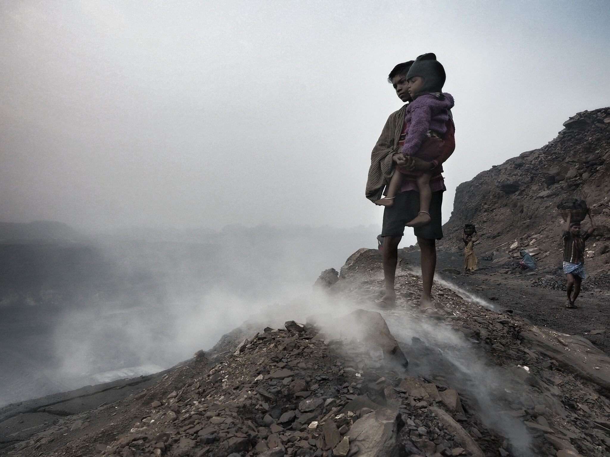 A young boy holds his baby brother on the edge of the Alkusha mine at Ganshadih.