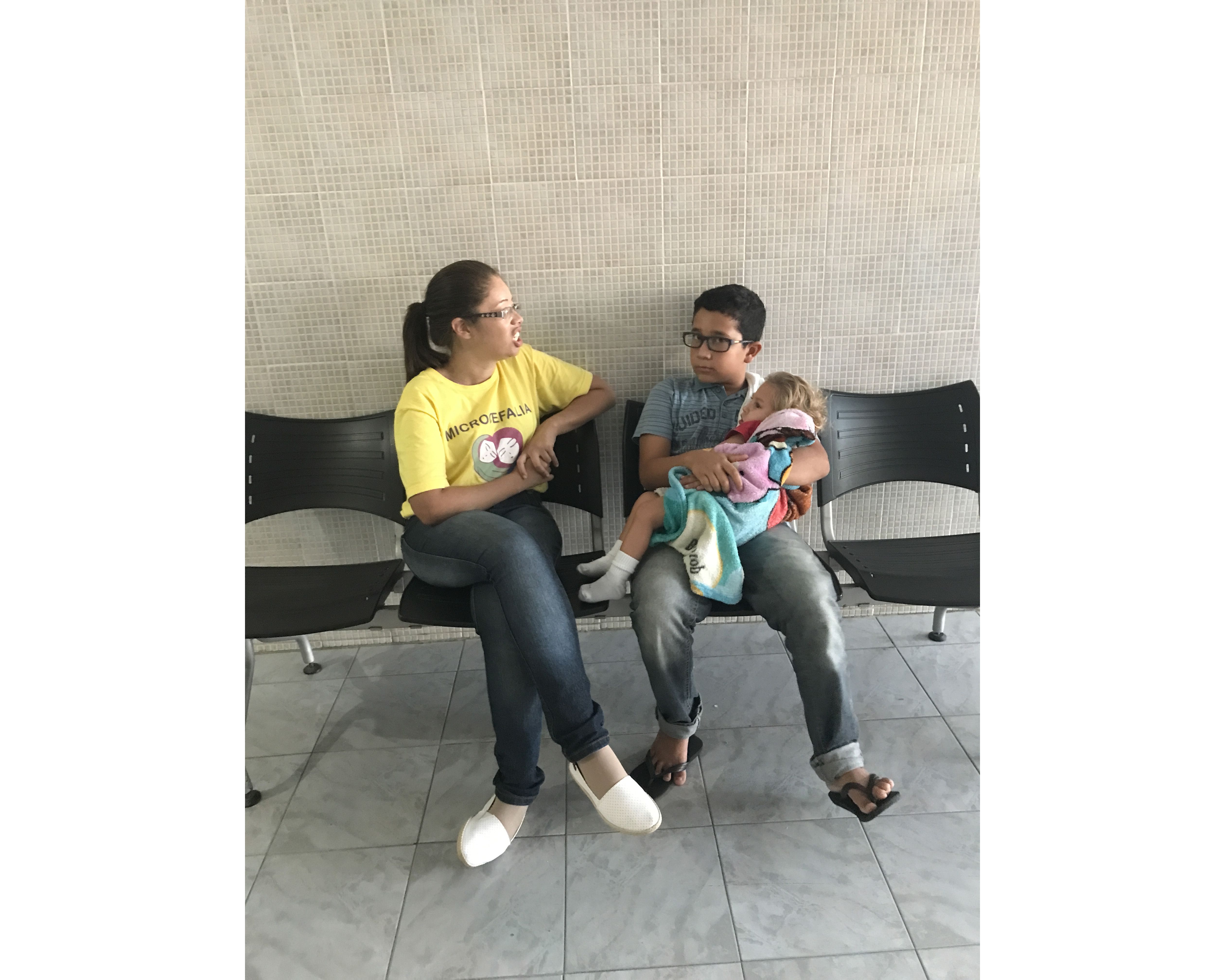 Marcos, 10, holds Gilberto and chats with others at the IPESQ clinic while waiting for his mother. “I feel like her helper,” he says to me. “If I wasn’t in my mother’s life, how would she do this all right now? I help a lot with Gilberto.” Marcos fantasizes about traveling to China. When I asked why, he said, “because it’s on the other side of the world from Brazil.” Image by Poonam Daryani. Brazil, 2017.