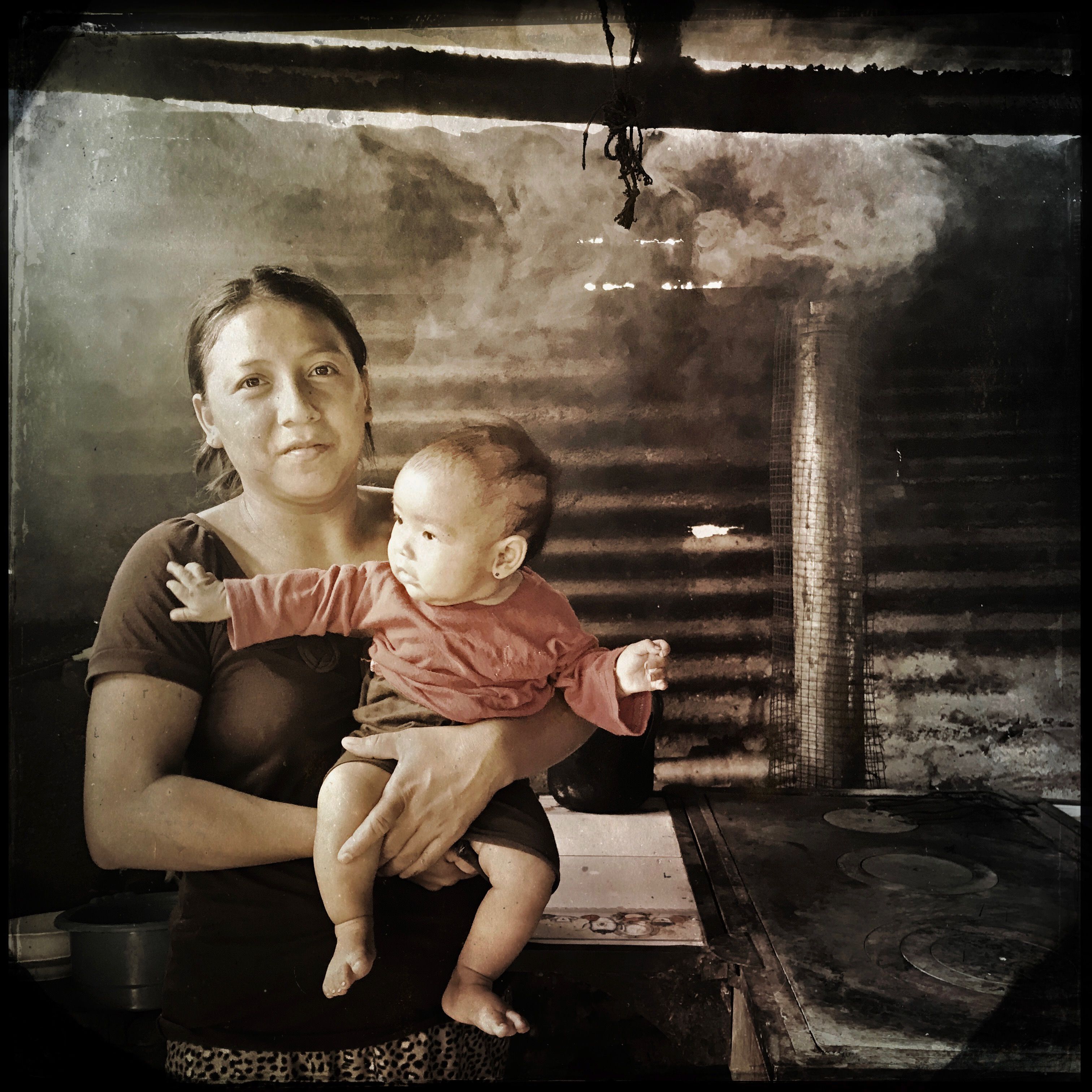 In Las Brisas, Guatemala, Yeni Contreras, 24, holds her four-month-old daughter Heidi. When she received an efficient wood-burning stove from the aid group Stove Team International, she carried it to her kitchen herself, piece by piece. She loves the stove, but, like many of her neighbors, she is afraid to cut a hole in the roof for the chimney, fearing the chimney will be damaged during the rainy season. Photo by Lynn Johnson. Guatemala, 2017.