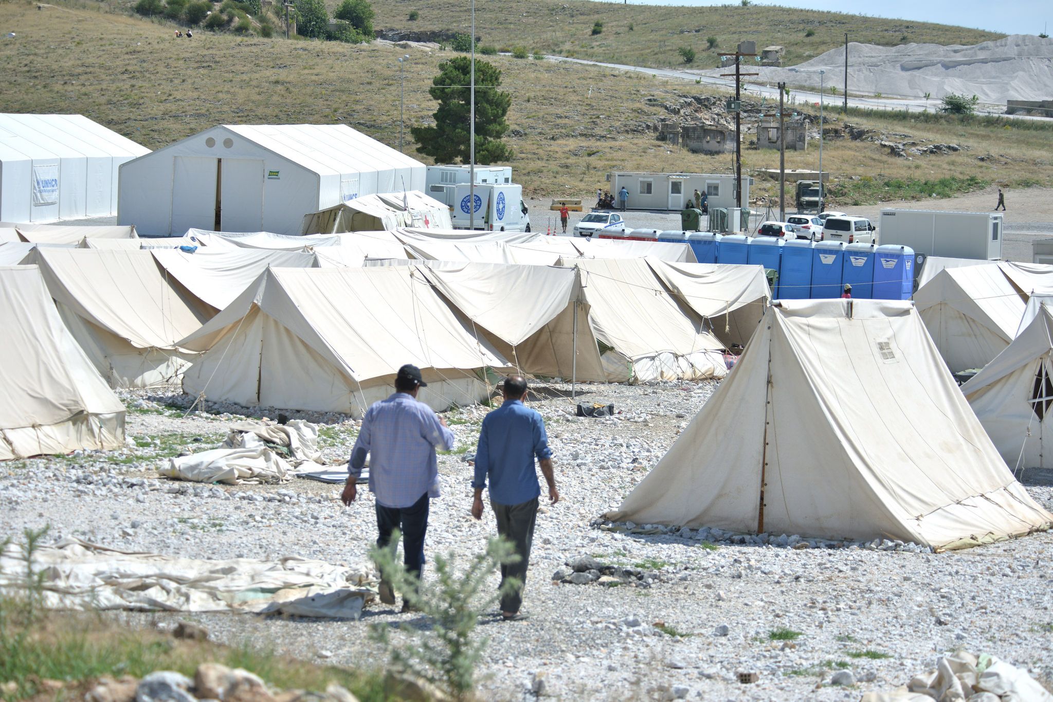 Many were evacuated to camps like this one, in Larisa, Greece. It’s located on a fenced gravel lot dotted with tents, off the side of a divided highway lined by fields the color of sand, over three-hours drive from Athens in one of the hottest, driest parts of the country. More than 800 Afghans and Syrians were deposited here, in the middle of nowhere, by government busses months ago, with no information on why or for how long. Image by Frederick Atax.
