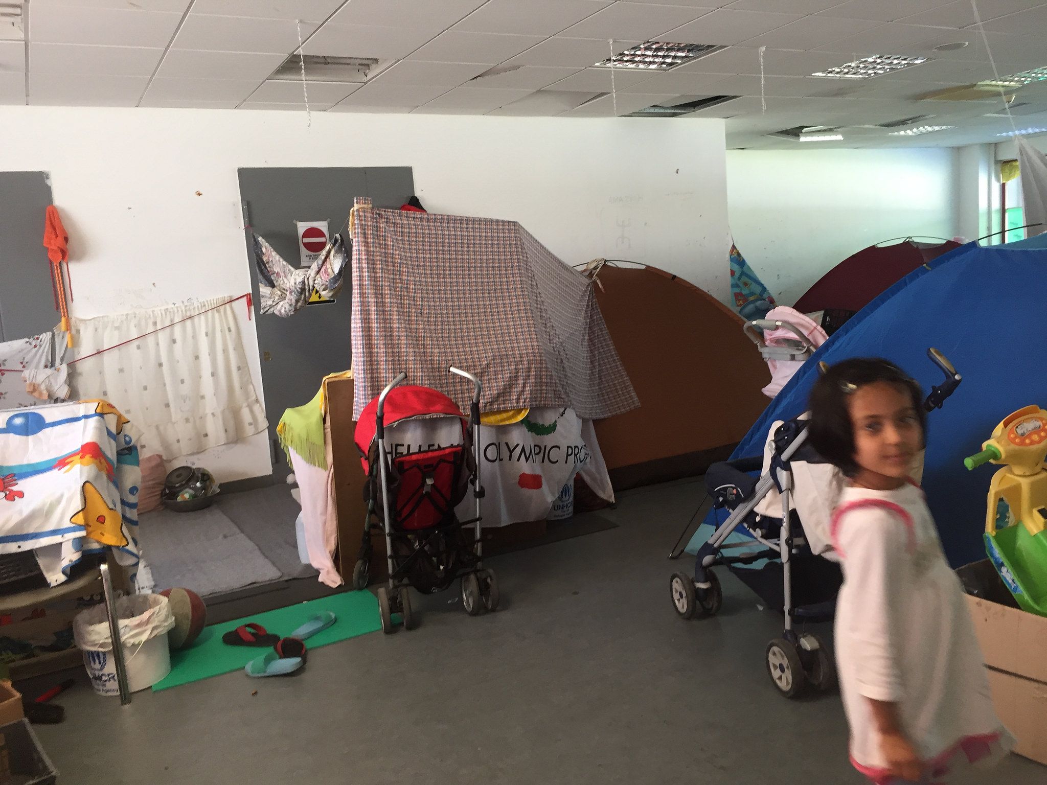 About fifty people including families with children lived in this room, in a mix of tents and make-shift enclosures made with sheets and blankets. Image by Sonia Shah. Greece, 2016.