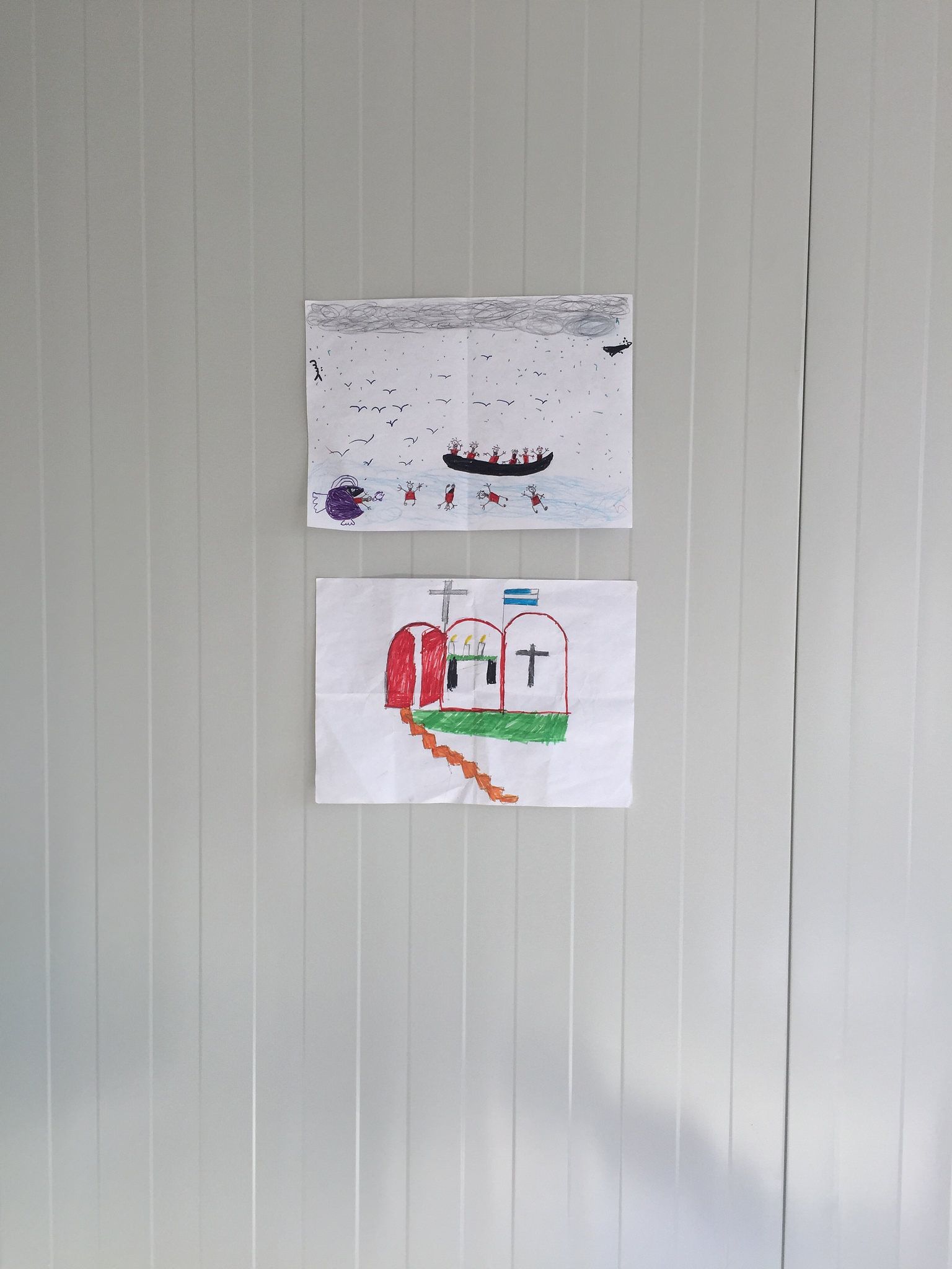 These are drawings by 14-year-old Sayeed, taped to the bare walls of a container stationed at the camp. Sayeed was planning to study engineering when he fled Kabul to escape recruitment by the Taliban. His drawing depicts a boat in the water surrounded by drowning people and sharks, a portrayal of his crossing over the Mediterranean. Over a dozen of the residents of this camp are unaccompanied minors like Sayeed. Image by Sonia Shah. Greece, 2016.