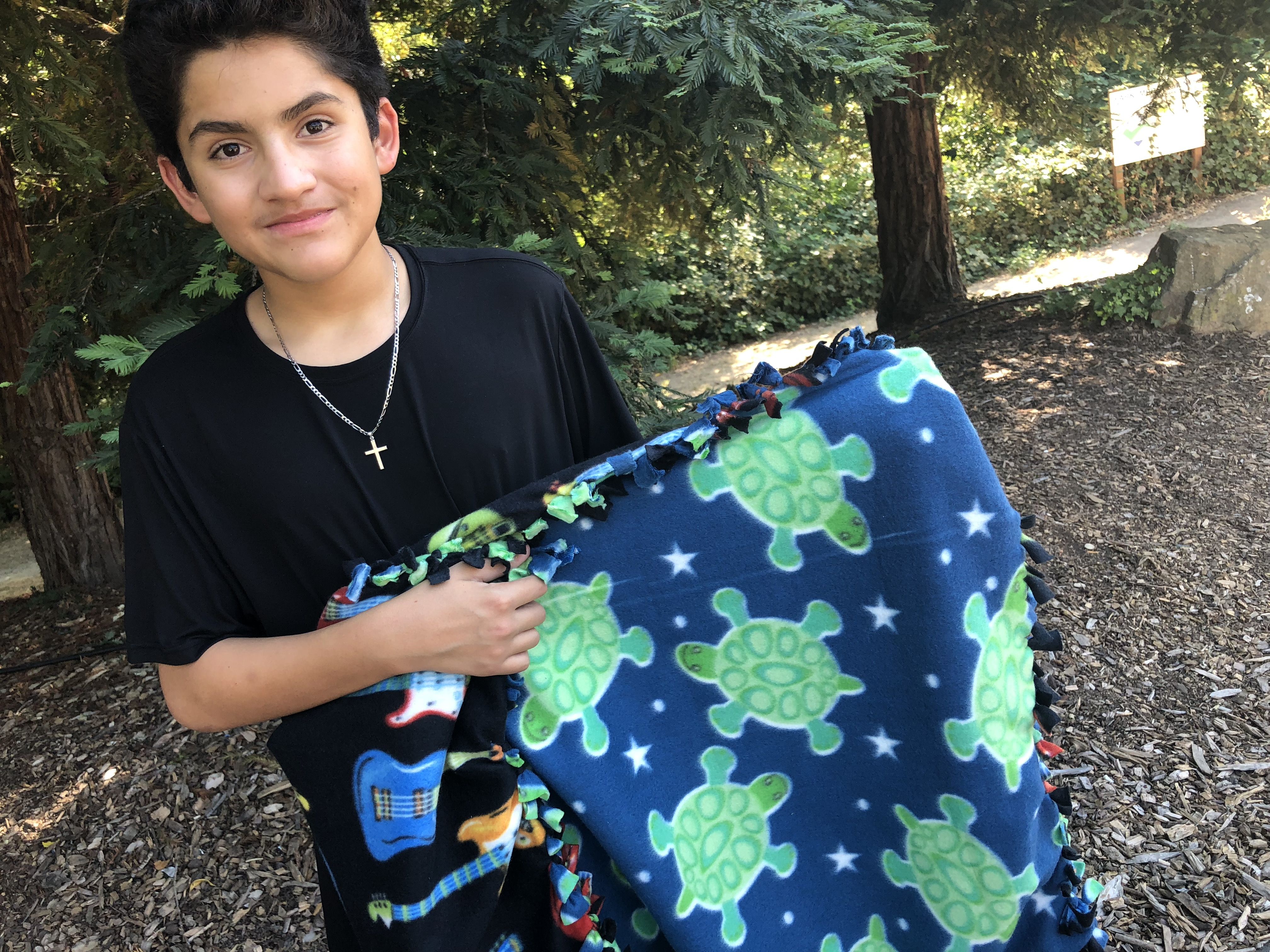 Carlos shows off a blanket he made with his mom. He chose the fabric with the guitars to reflect his love of music. His mom picked the sea turtles. Image by Jaime Joyce for TIME Edge. California, 2018.