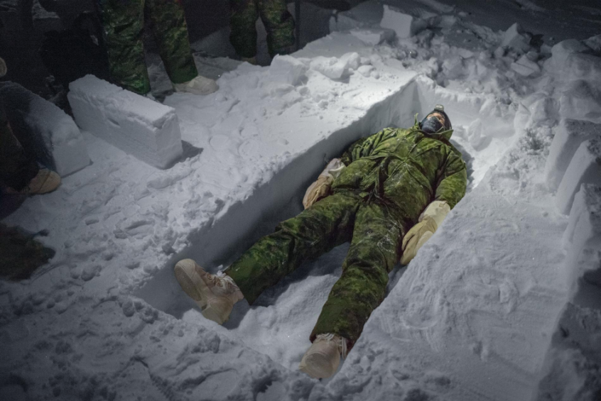 Canadian aviator Simon Jean stretches out in a fighter trench he has begun to dig by cutting out blocks of ice. The trenches can serve as basic shelters, and the ice blocks can also be used for building igloos. Image by Louie Palu. Canada, 2019.