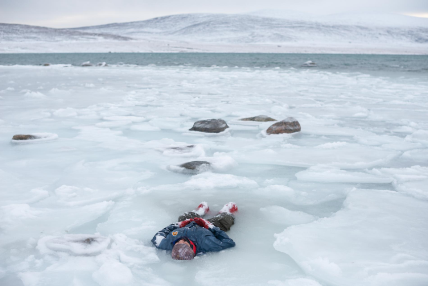 A Canadian ranger lies in a pool of icy slush and water during training for search-and-rescue operations on Baffin Island. His fellow rangers must quickly get him into dry clothes and raise his body temperature before hypothermia sets in. Image by Louie Palu. Canada, 2019.